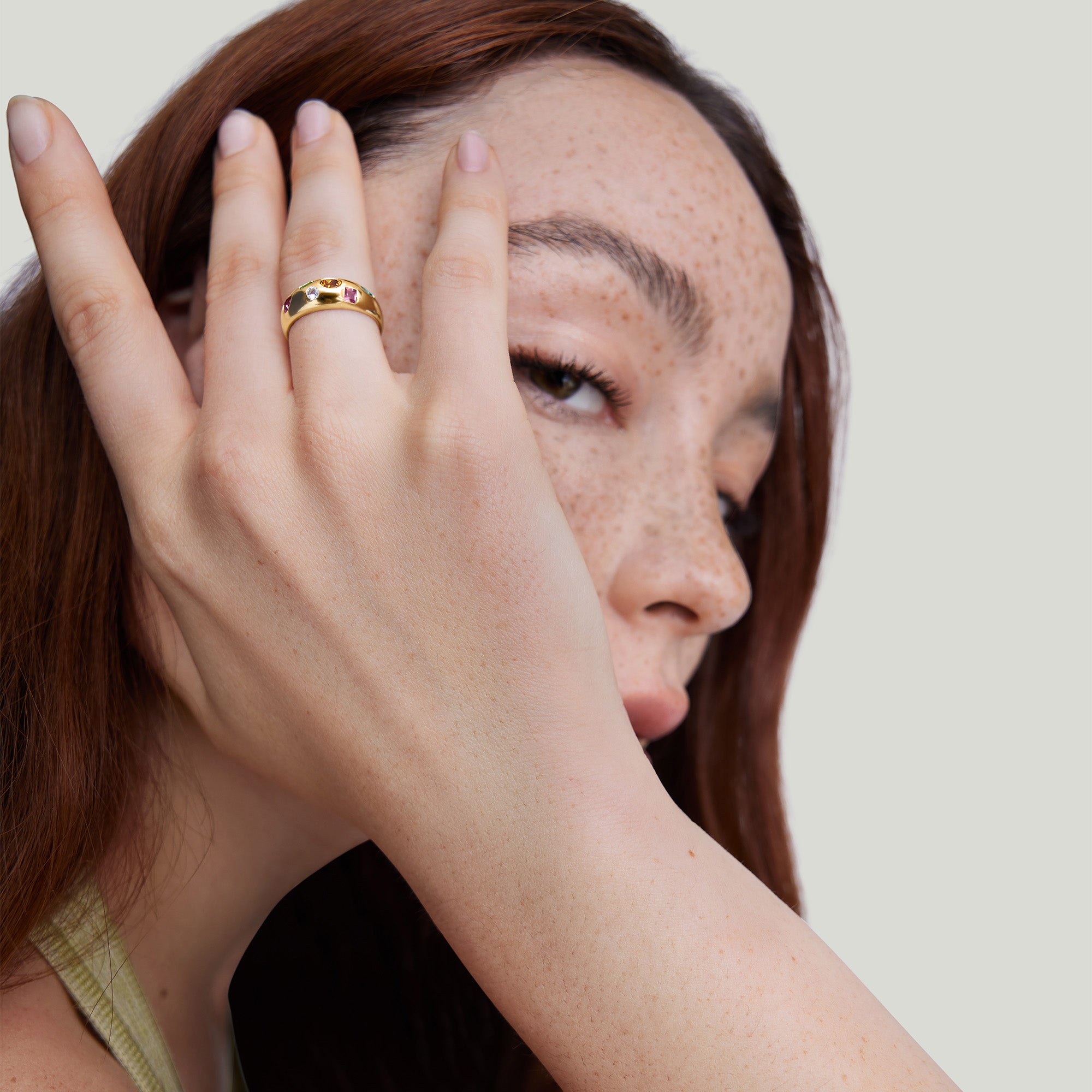Woman with freckles showcasing the Toronto Mosaic DÃ´me Ring featuring six multicolored gemstones on her finger.