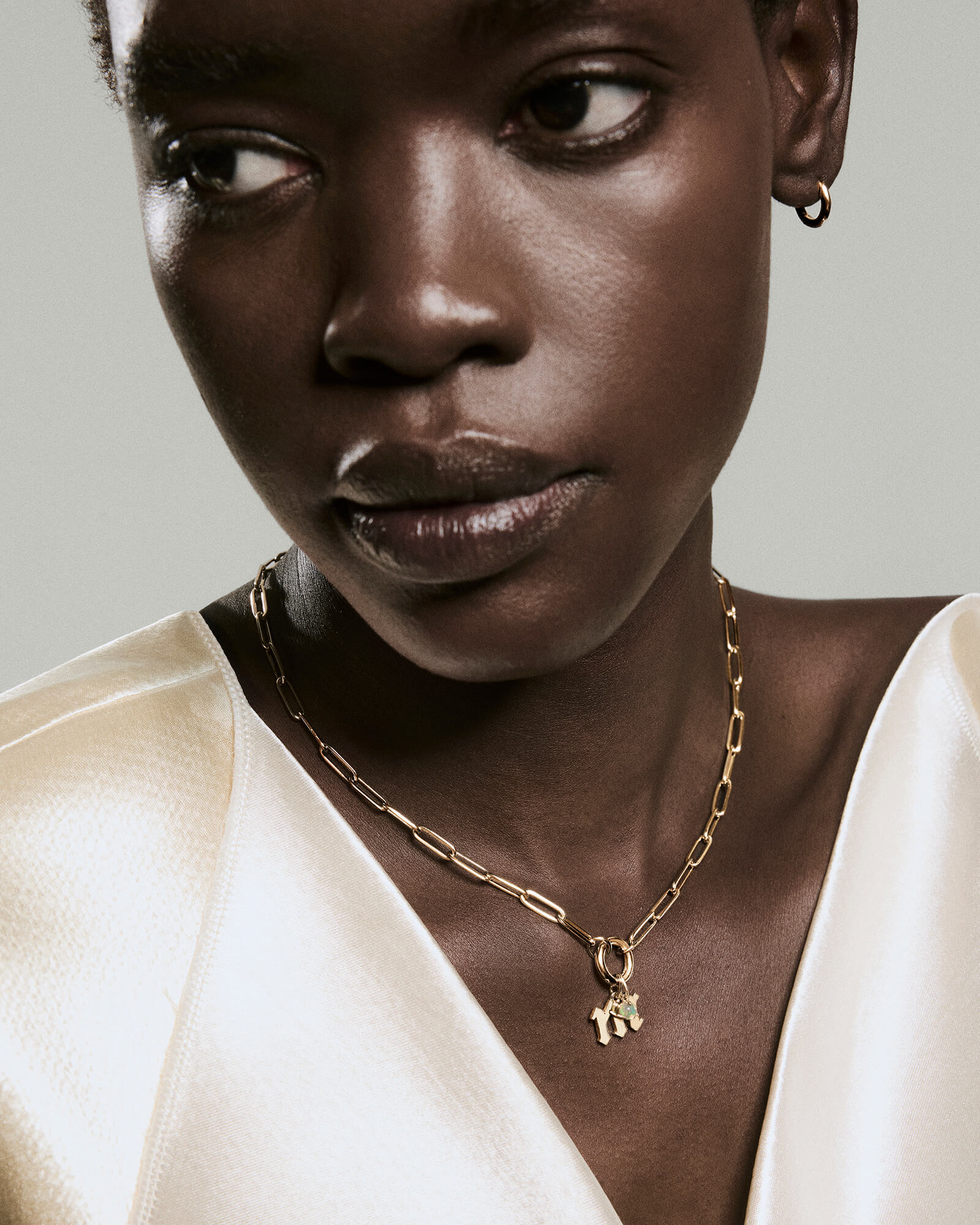 Close-up of a person wearing a Gothic Letter Pendant on a chunky gold chain, paired with a gold hoop earring, highlighting the pendant's edgy style.