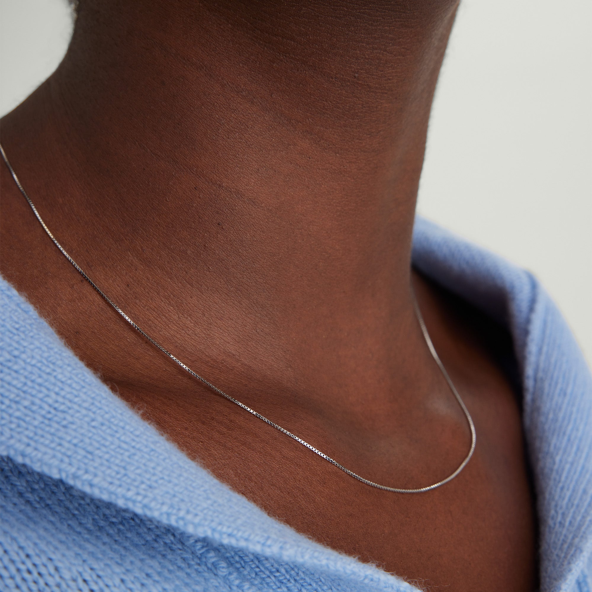 Baby Box Chain Necklace worn by a person, showcasing its lightweight design and light-catching qualities. Close-up emphasizes the classic box chain details.