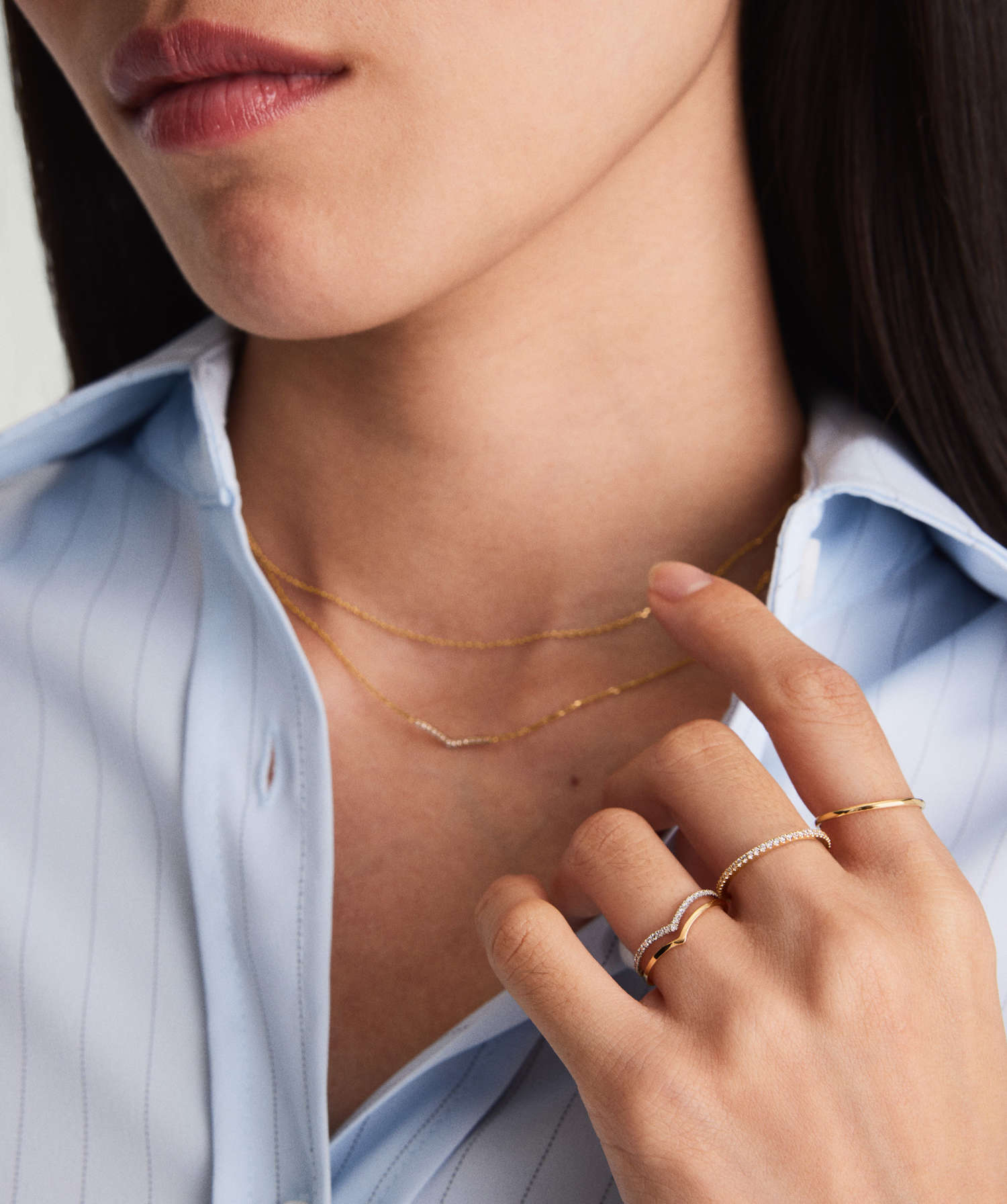 Wishbone Stacker Set adorning a woman's hand, featuring delicate gold rings and a chain, highlighted in a close-up of her neck and lips.