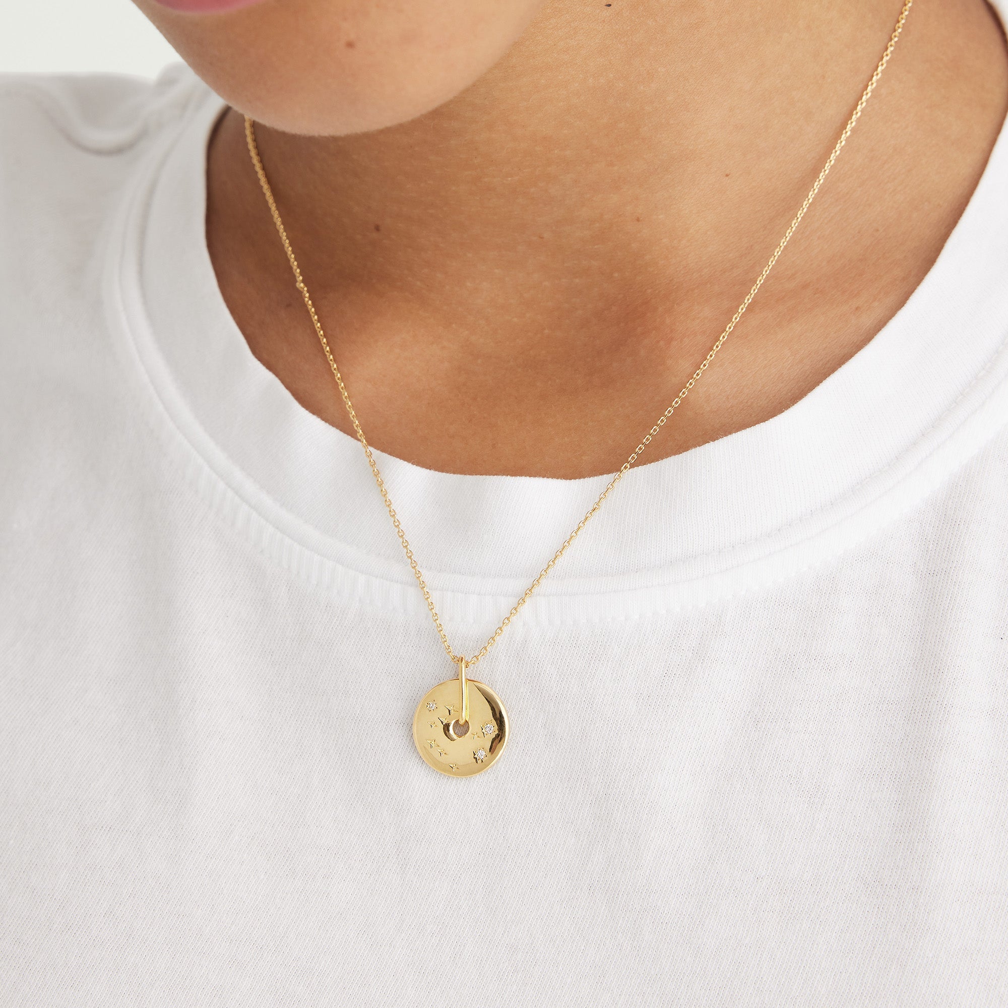 Person wearing the Zodiac Pendant Necklace, an 18k gold vermeil with a spinning disk and white sapphire gemstones, showcasing a constellation design.