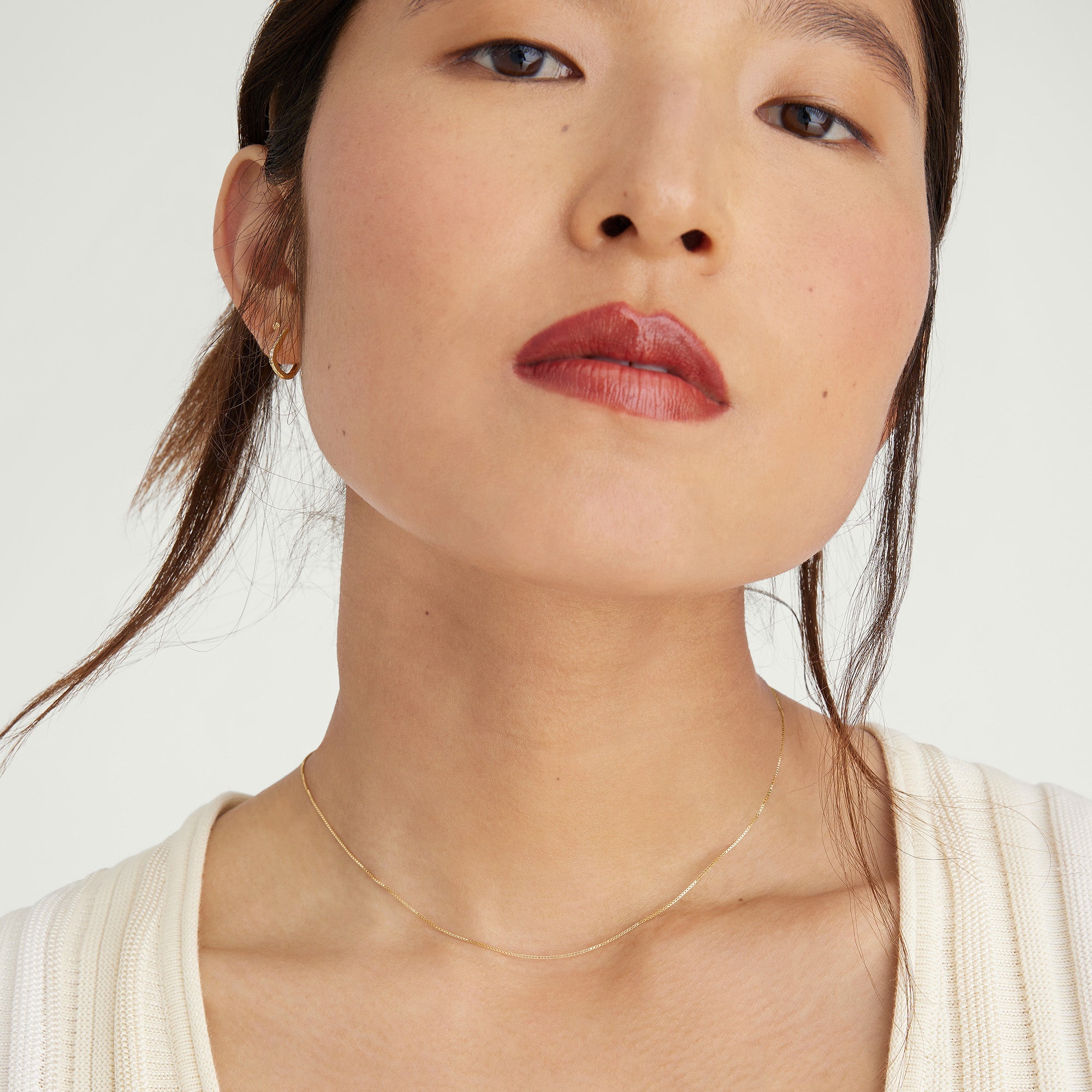 Baby Box Chain Necklace showcased on a woman with red lipstick. The light, classic gold necklace elegantly complements her look, highlighting the necklace's delicate craftsmanship.
