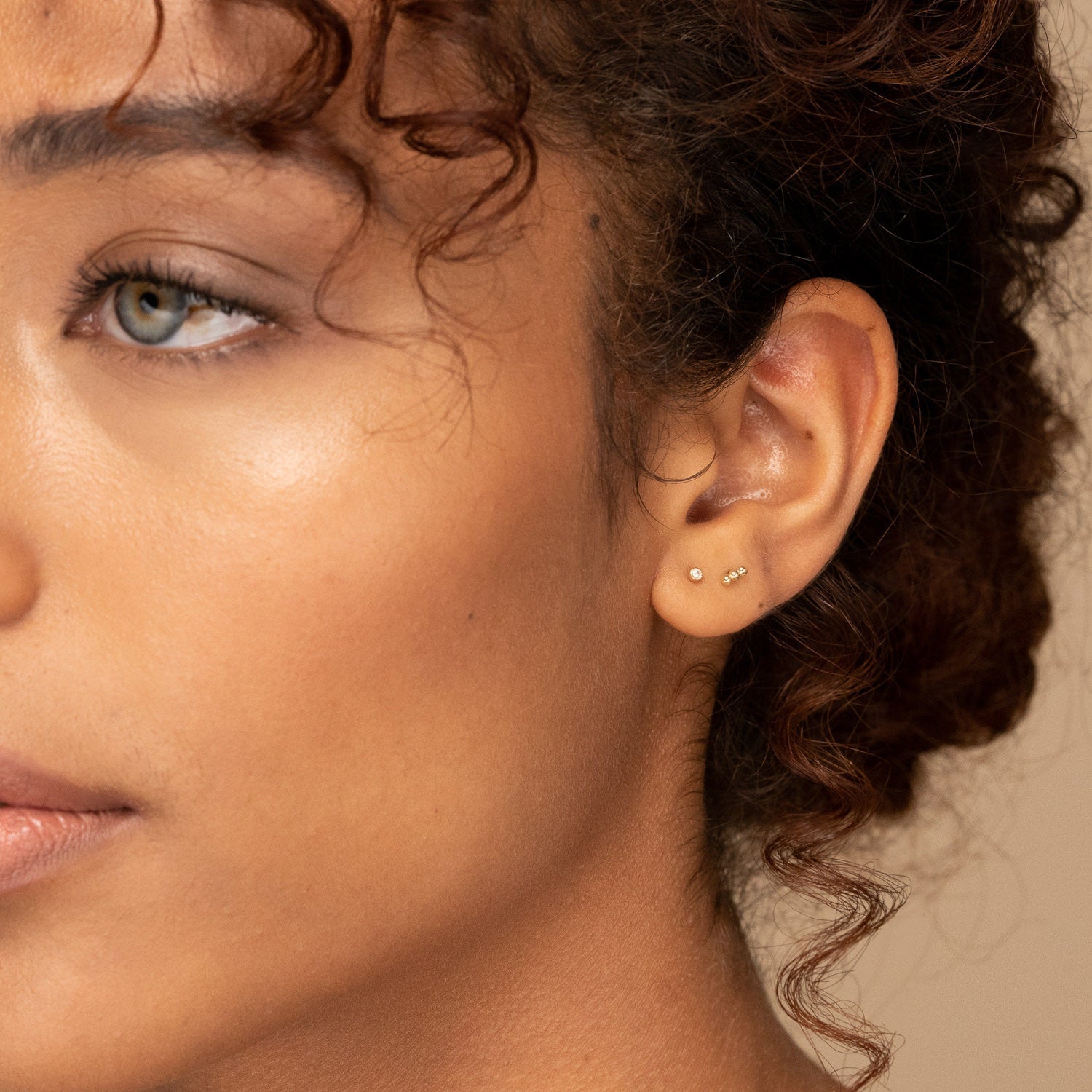 Single Tiny Diamond Stud adorning a woman's ear, showcasing a delicate, handcrafted 14k solid gold setting with an ethically sourced diamond.