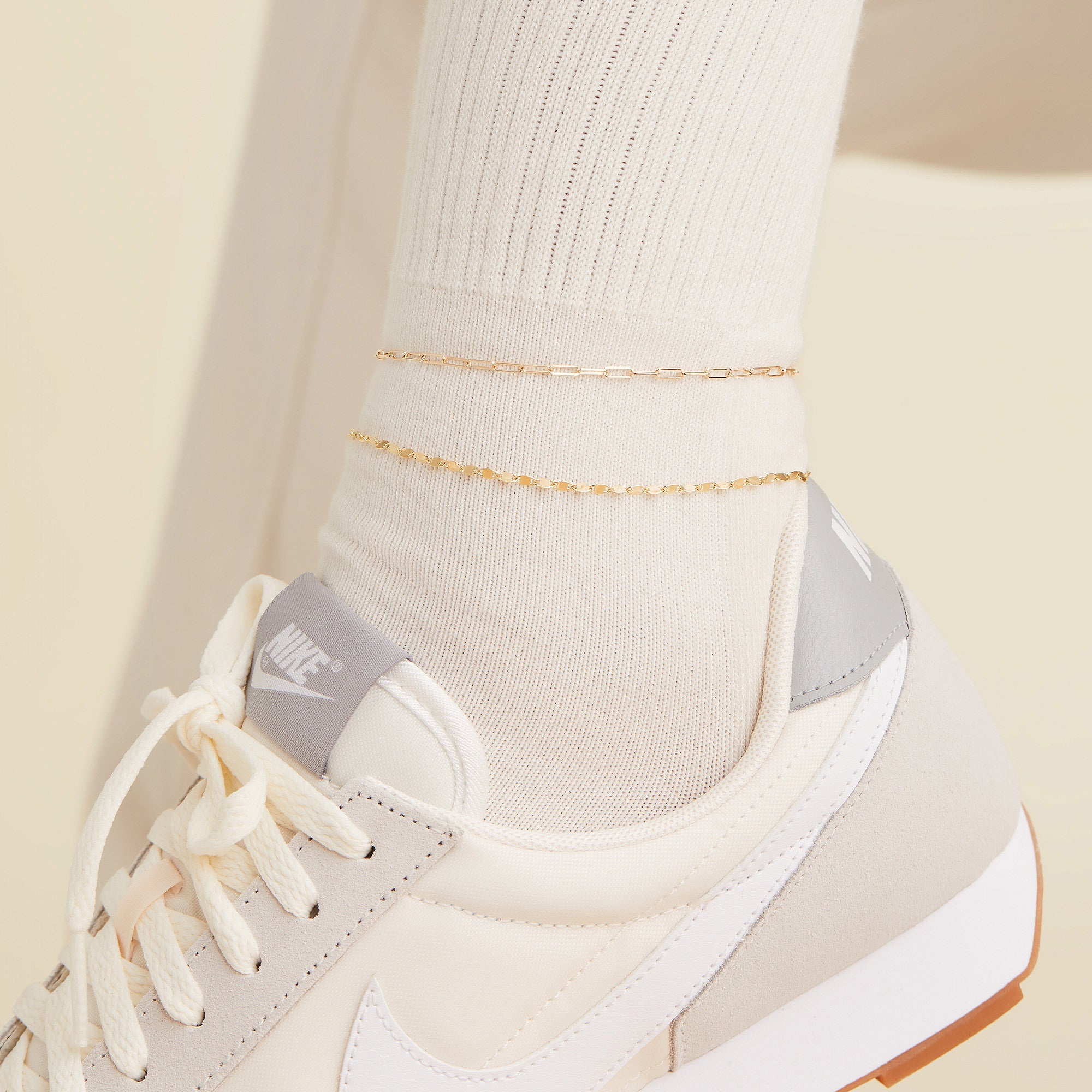 Anchor Chain Anklet: A close-up of a foot wearing a white sock, white tennis shoe, and a 14k solid gold chain anklet with interconnected links.