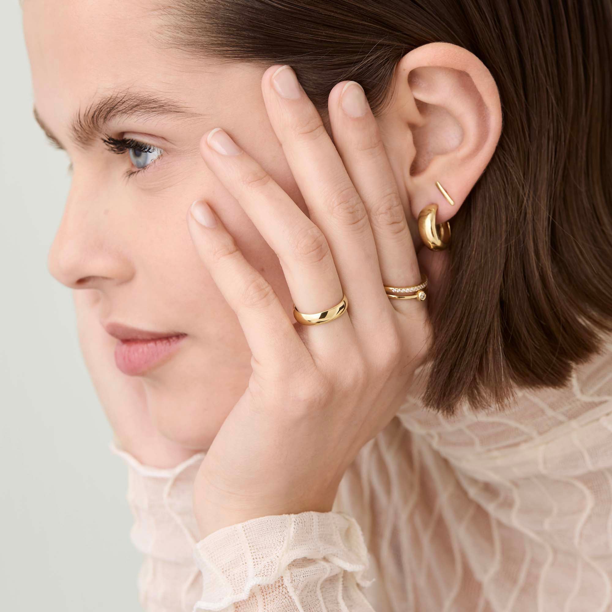 Close-up of a womanâs face with a 4mm Curve Band gold ring on her finger, highlighting the ring's elegance and lightweight design.