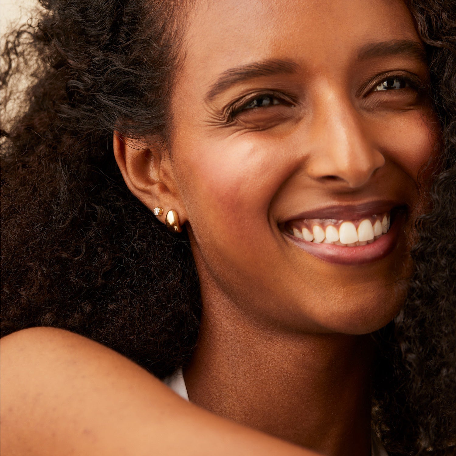 Woman smiling, showcasing Mejuri DÃ´me Huggies earrings with a sleek, sculptural design, hugging the earlobe, perfect for stacking and everyday wear.