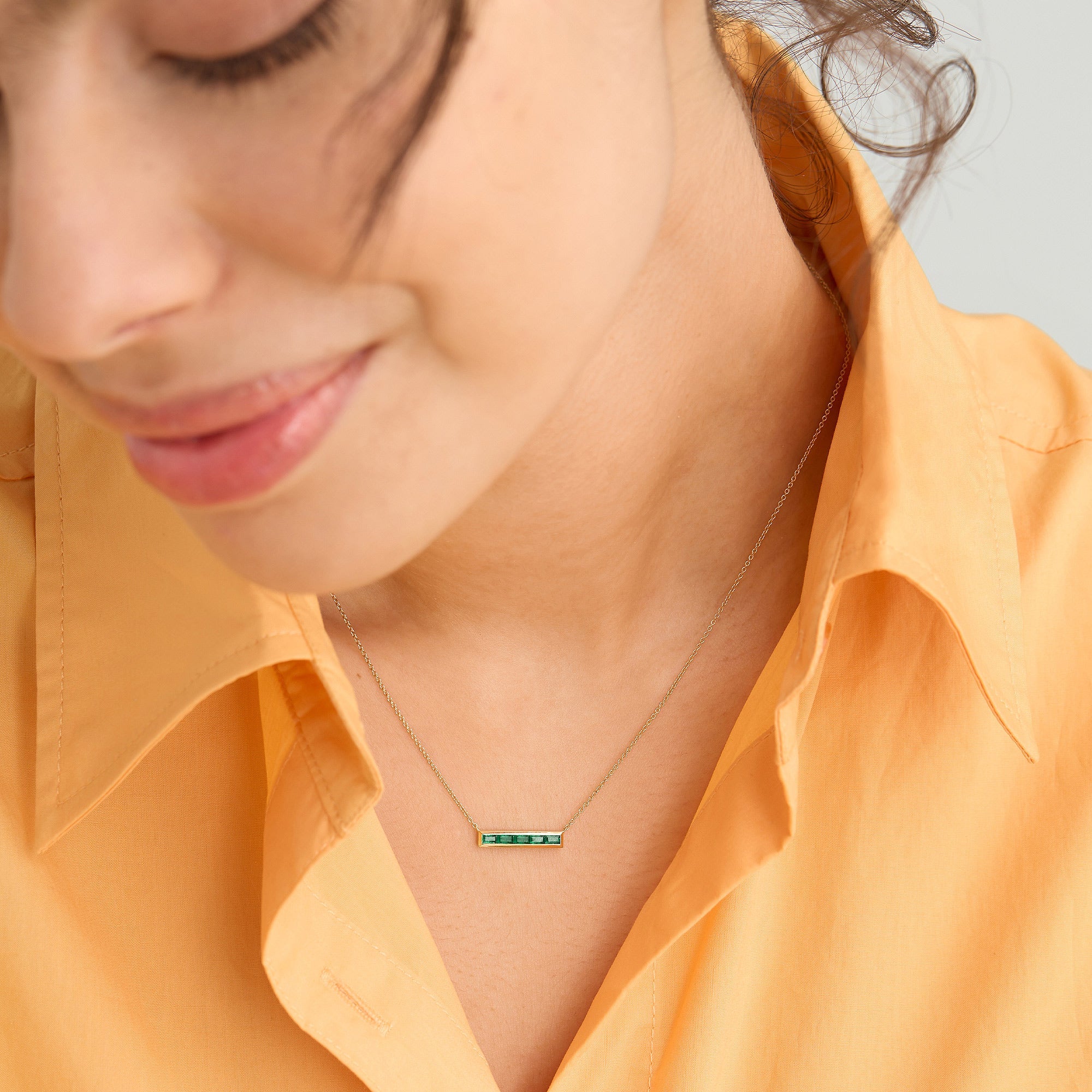 Woman wearing a Baguette Emerald Bar Necklace in 14k solid gold with handcrafted baguette emeralds, each with unique inclusions.