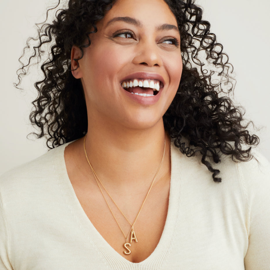 Woman with curly hair wearing a white v-neck sweater and a Bold Letter Pendant Necklace in 18k gold vermeil, featuring a statement initial on a 20-22 inch cable chain.