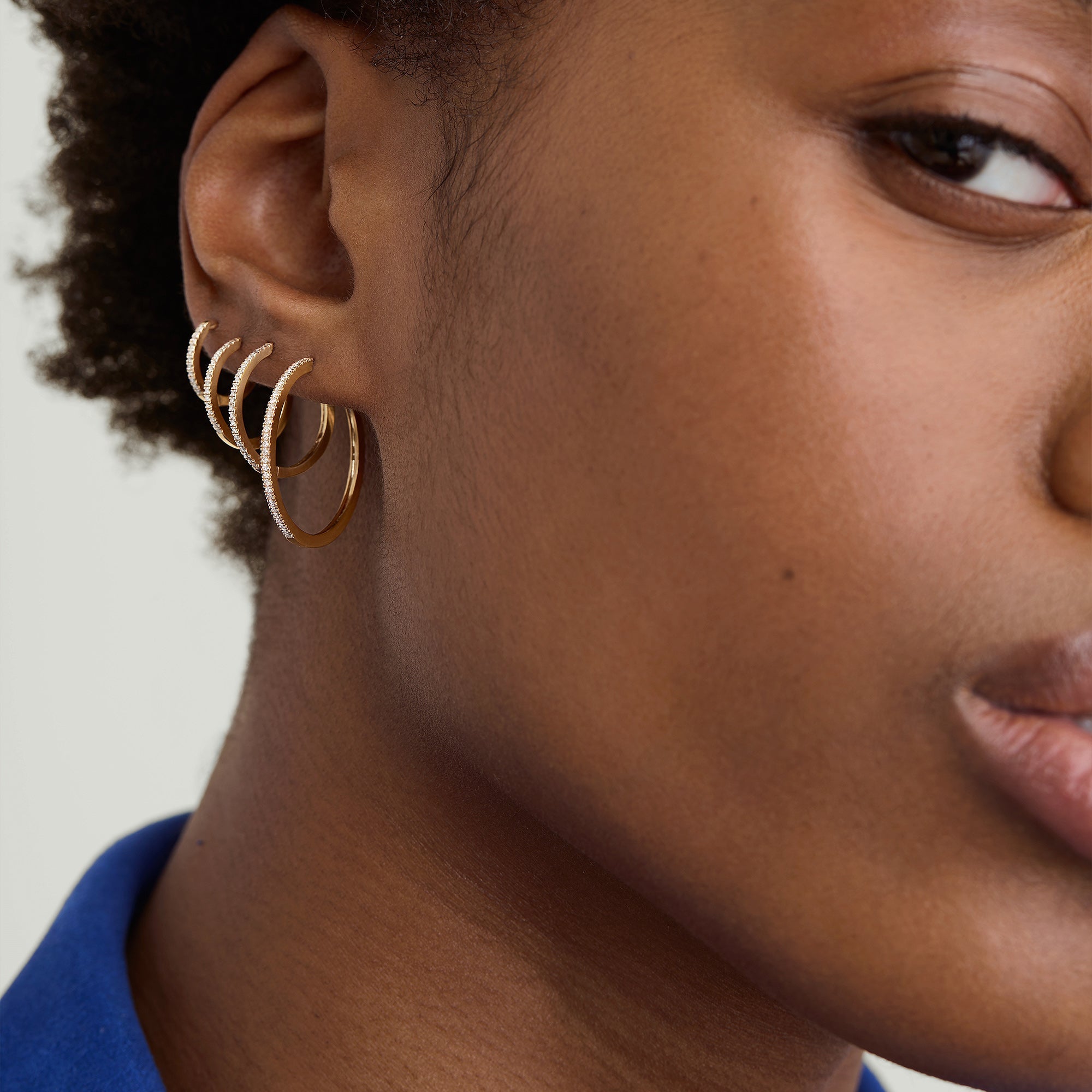 PavÃ© Diamond Large Hoops: Close-up of a woman's ear wearing handcrafted 14k solid gold hoops with pavÃ© diamonds.