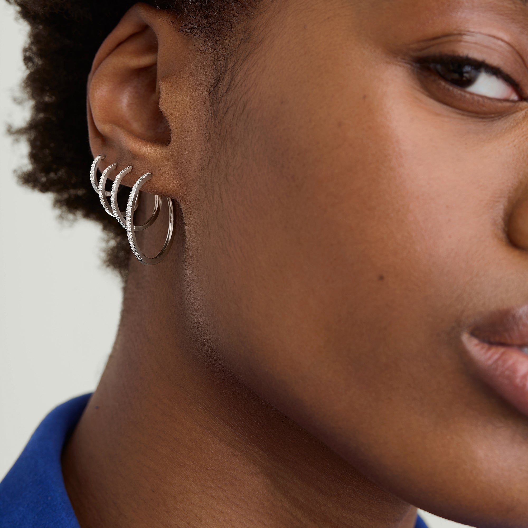 PavÃ© Diamond Huggie Hoops: Close-up of a woman's ear showcasing handcrafted, stackable diamond hoops in recycled 14k solid gold, worn in two versatile styles.
