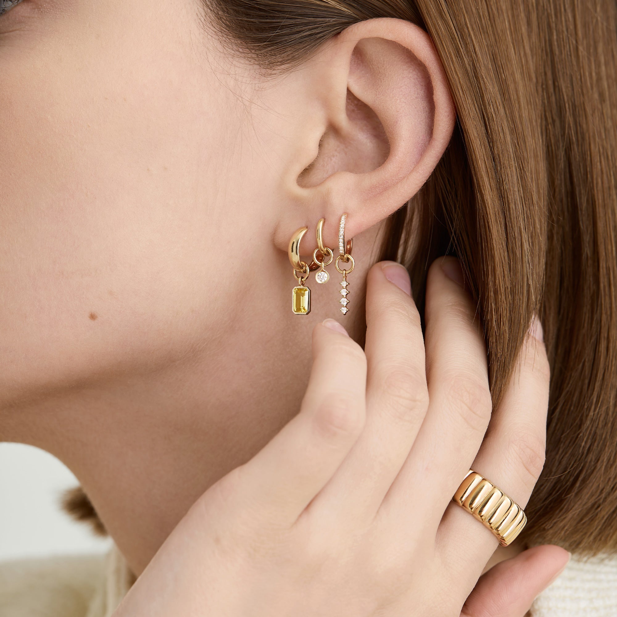 Woman wearing Single Diamond Icicle Hoop Charm on her ear, showcasing the elegant gold earring in a close-up view.
