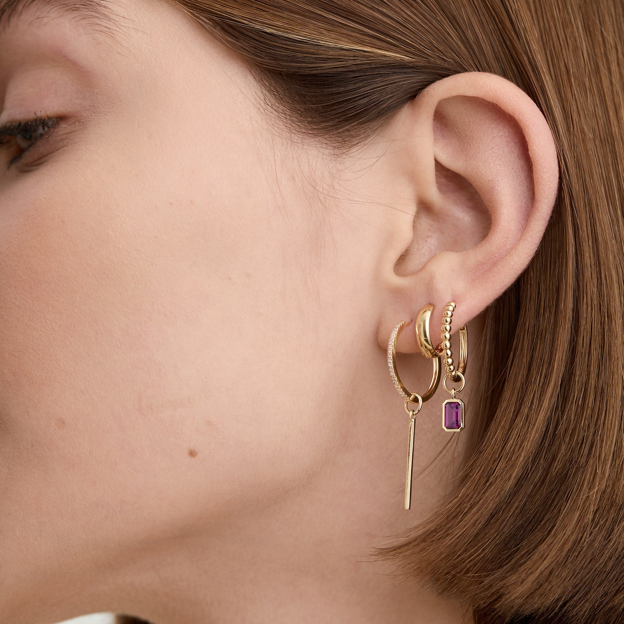Close-up of a woman's ear wearing a Single Bar Hoop Charm for personalizing everyday hoops with interchangeable charms.