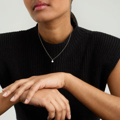 Woman wearing a black shirt showcasing the Mini Pearl Pendant Necklace, handcrafted in 18k gold vermeil with freshwater pearls, highlighting its elegant and versatile design.