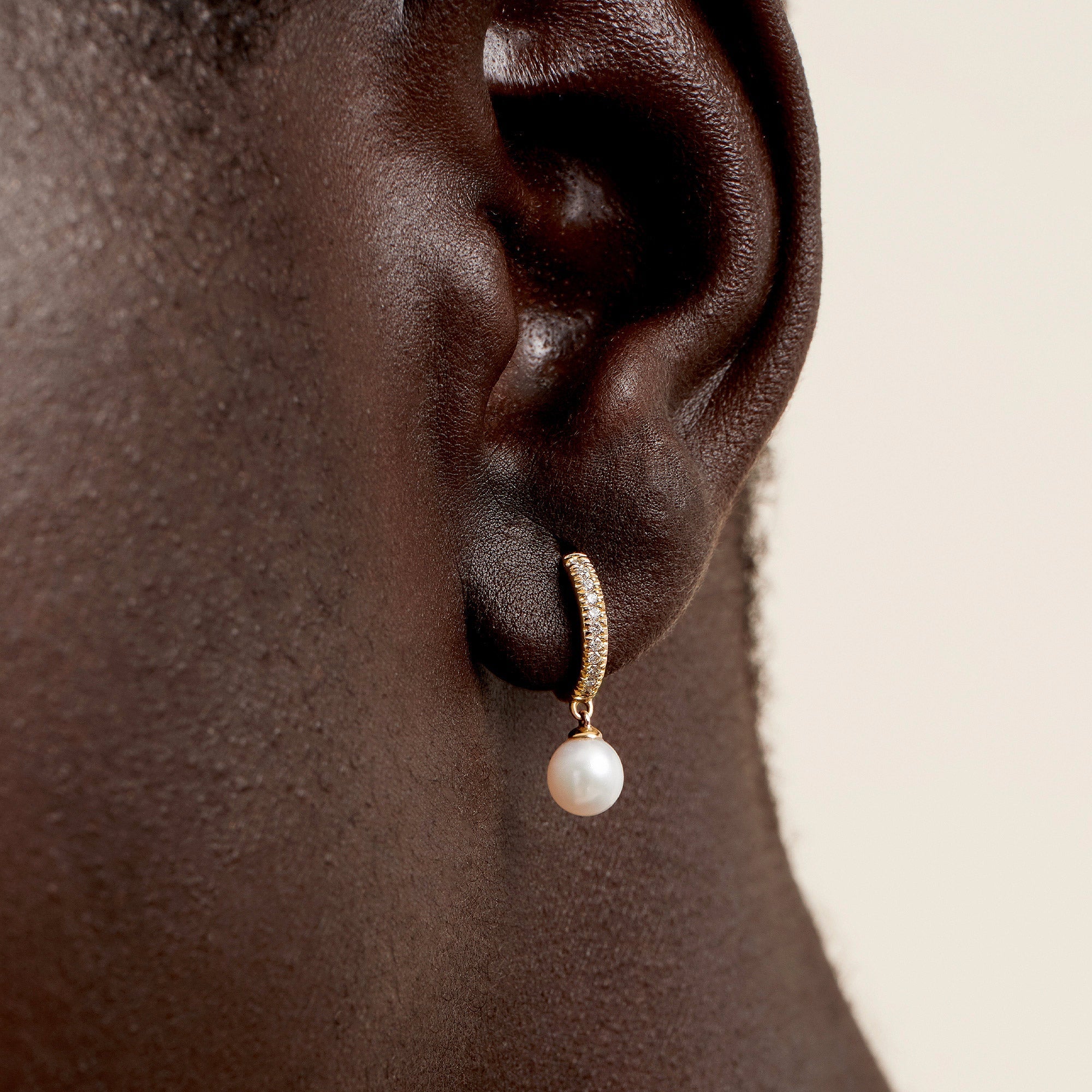 Close-up of an ear wearing PavÃ© Diamond Pearl Huggies, showcasing 14k gold earrings with 22 diamonds and a freshwater pearl.