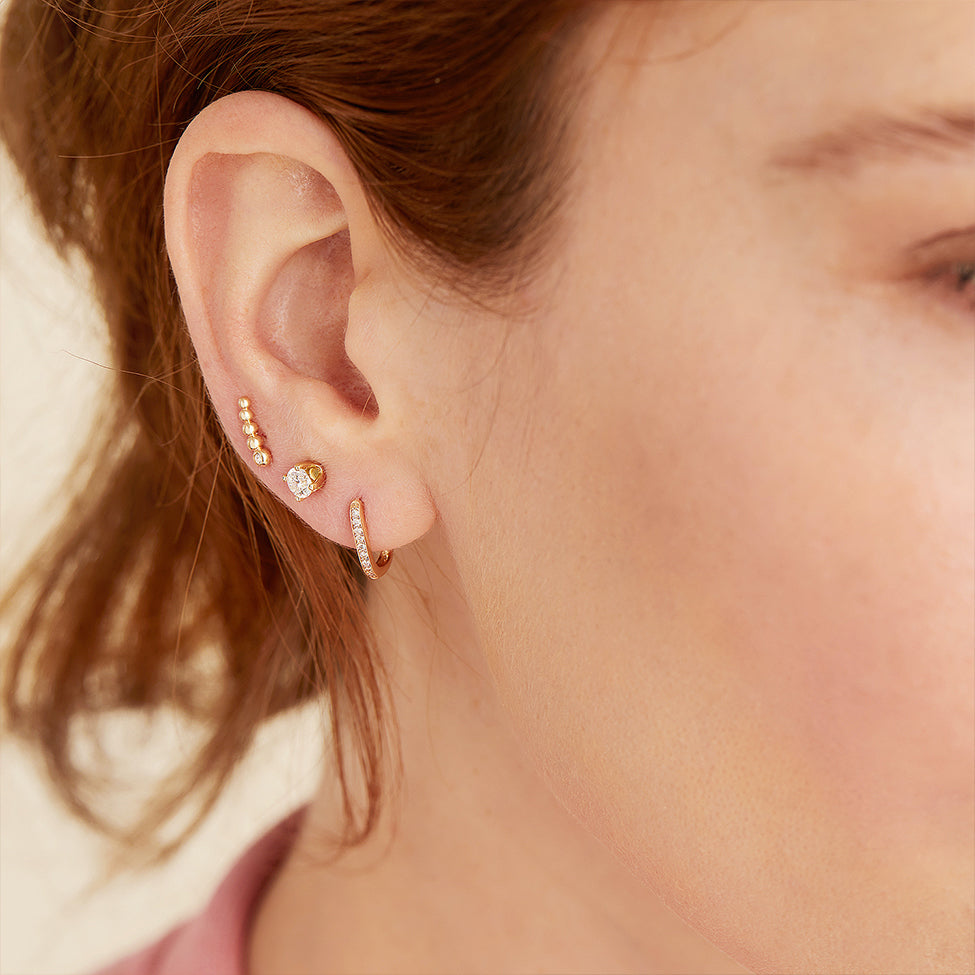 Close-up of a woman's ear adorned with a Single PavÃ© Diamond Huggie U Hoop, a sparkly handcrafted 14k solid gold earring with diamonds.