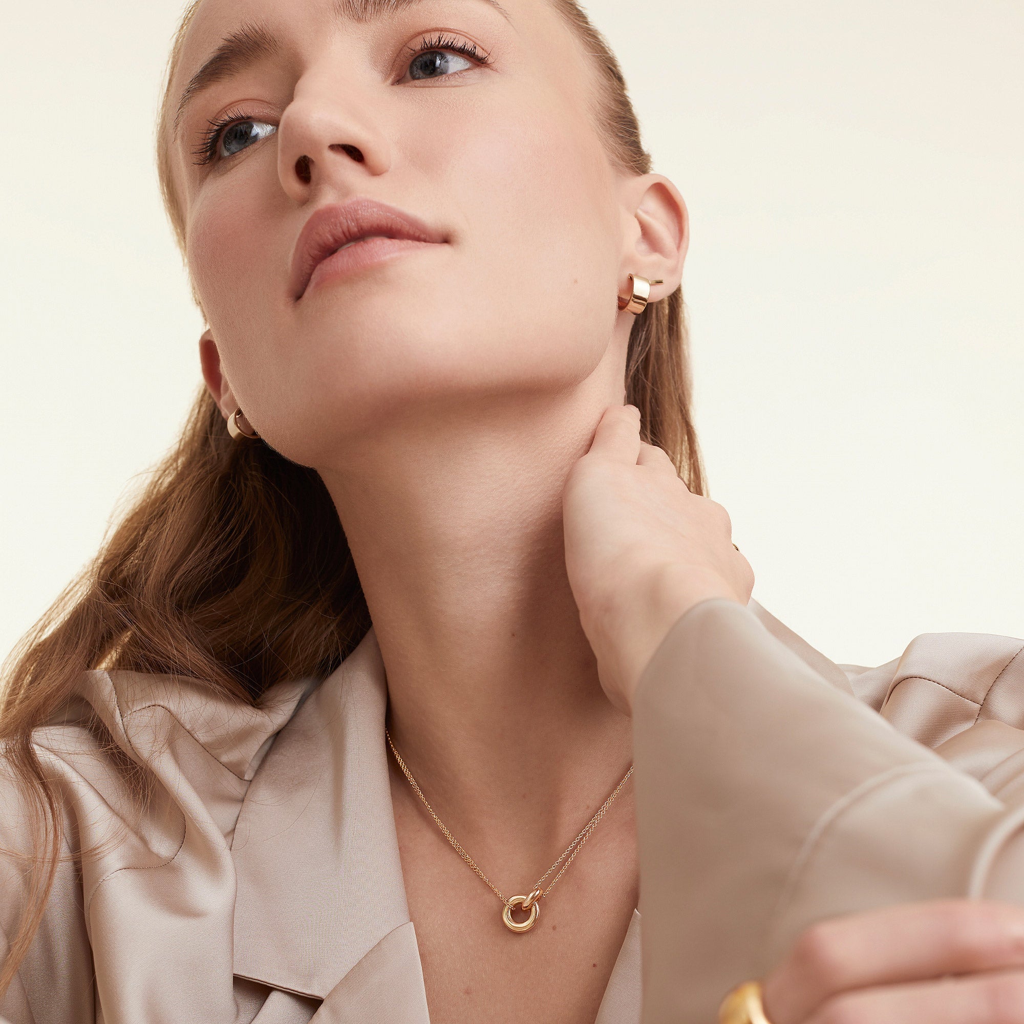 Woman touching her neck, showcasing a Vermeil Linked Necklace with two interlinked gold rings, symbolizing personal bonds, worn with matching earrings.