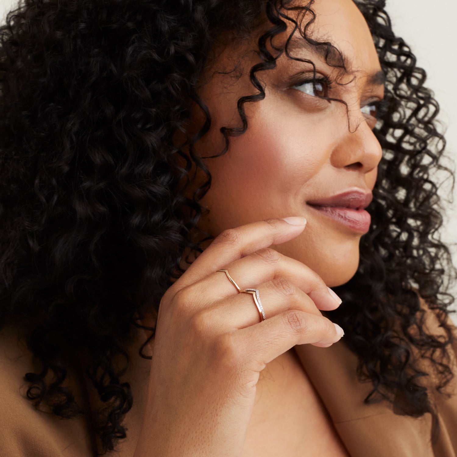 Woman with curly hair wearing a handcrafted 14k solid gold Wishbone Ring on her finger, showcasing its elegant design as a good luck charm and stacker.