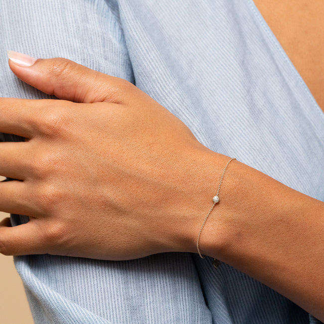 Person wearing the Solo Diamond Bracelet, featuring a solid gold band and a bezel-set round diamond on their wrist.