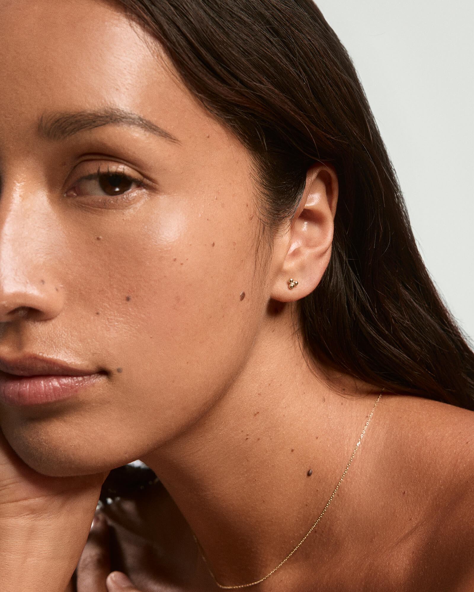 Close-up of a young woman's face highlighting Spheres Cluster Studs, a small gold stud earring, complementing her warm complexion and relaxed expression.