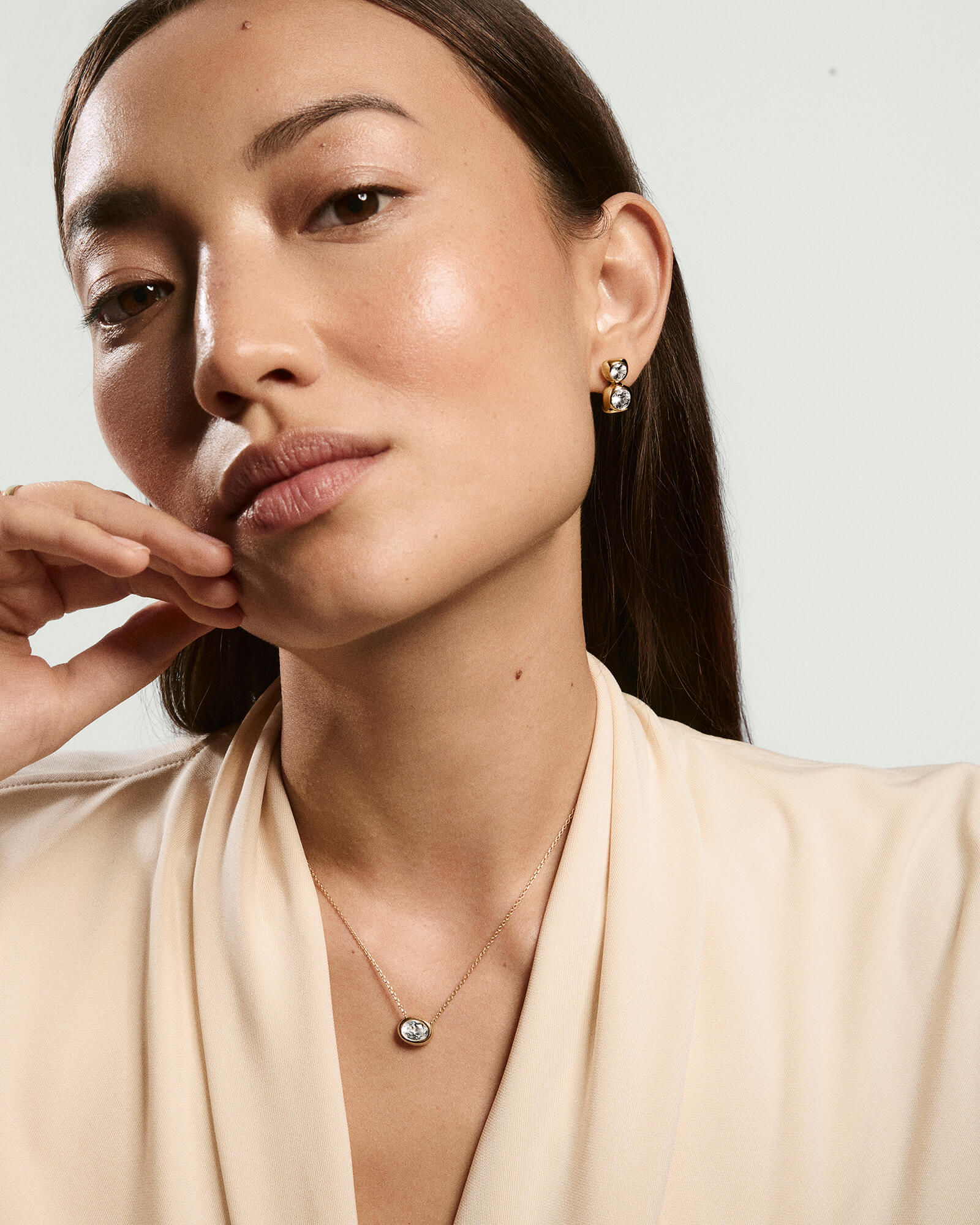 Young woman wearing the Lucia Necklace, featuring a delicate gold chain and oval bezel-set lab grown sapphire, styled elegantly with matching gold earrings.