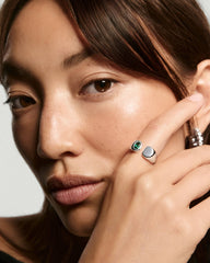 Young woman showcasing the Noa Open Signet Pinky Ring with a green gemstone set in a sleek, silver band, alongside another polished silver ring.