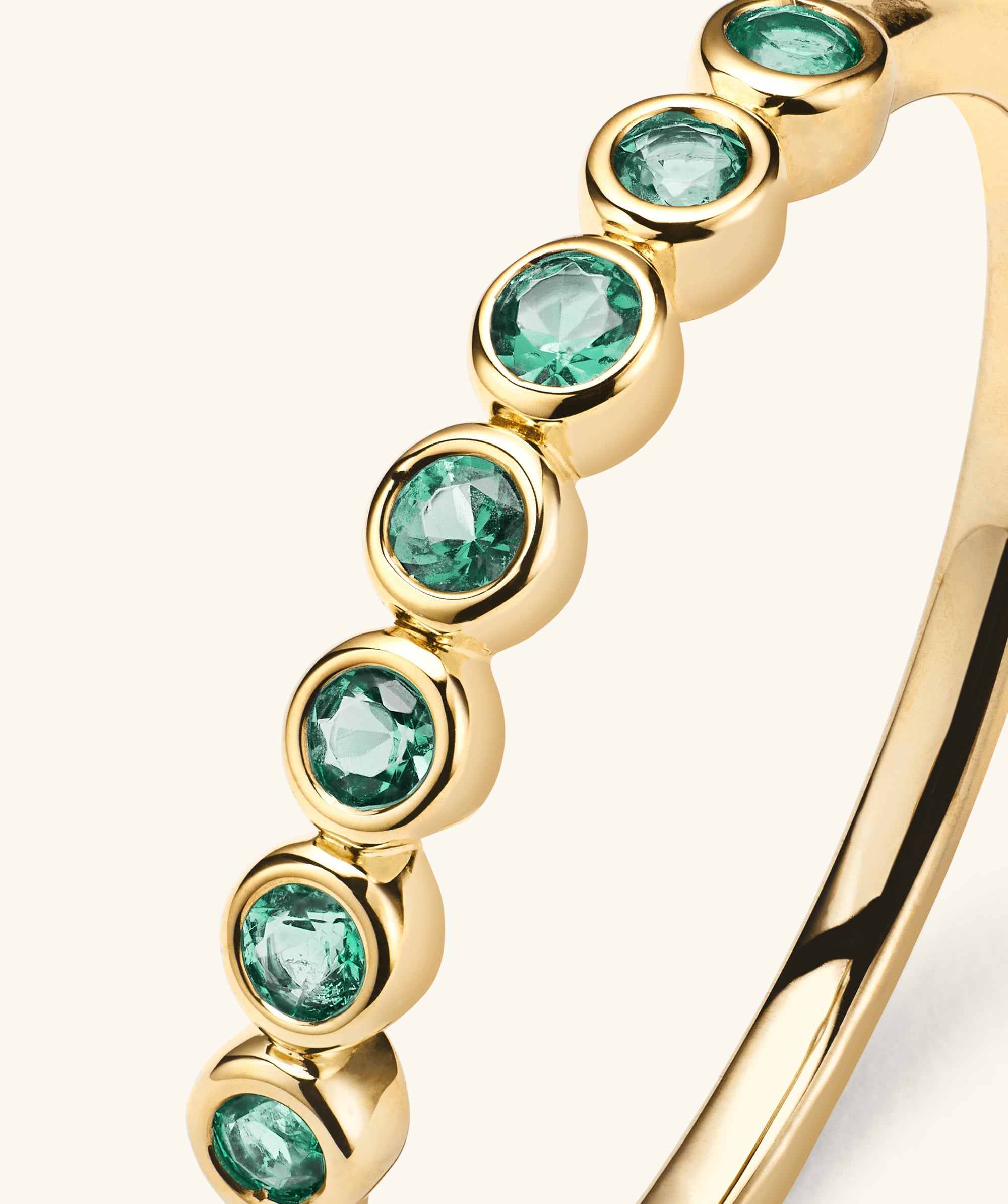 Bezel Emerald Half Eternity Band: 14k solid gold ring with bezel-set emerald gemstones, each gem uniquely characterized by natural inclusions.