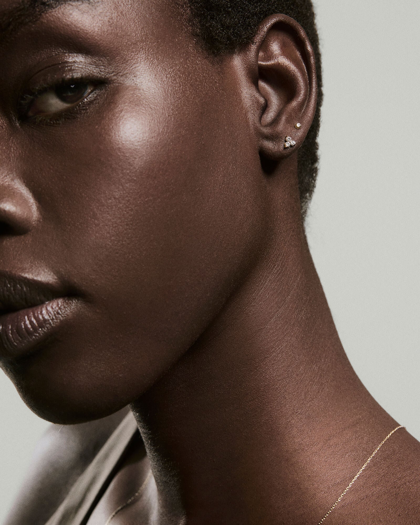 Close-up of an ear with the Diamond Lotus Flat Back Stud, featuring three sparkling diamonds set in 14k gold, alongside a delicate gold chain necklace.