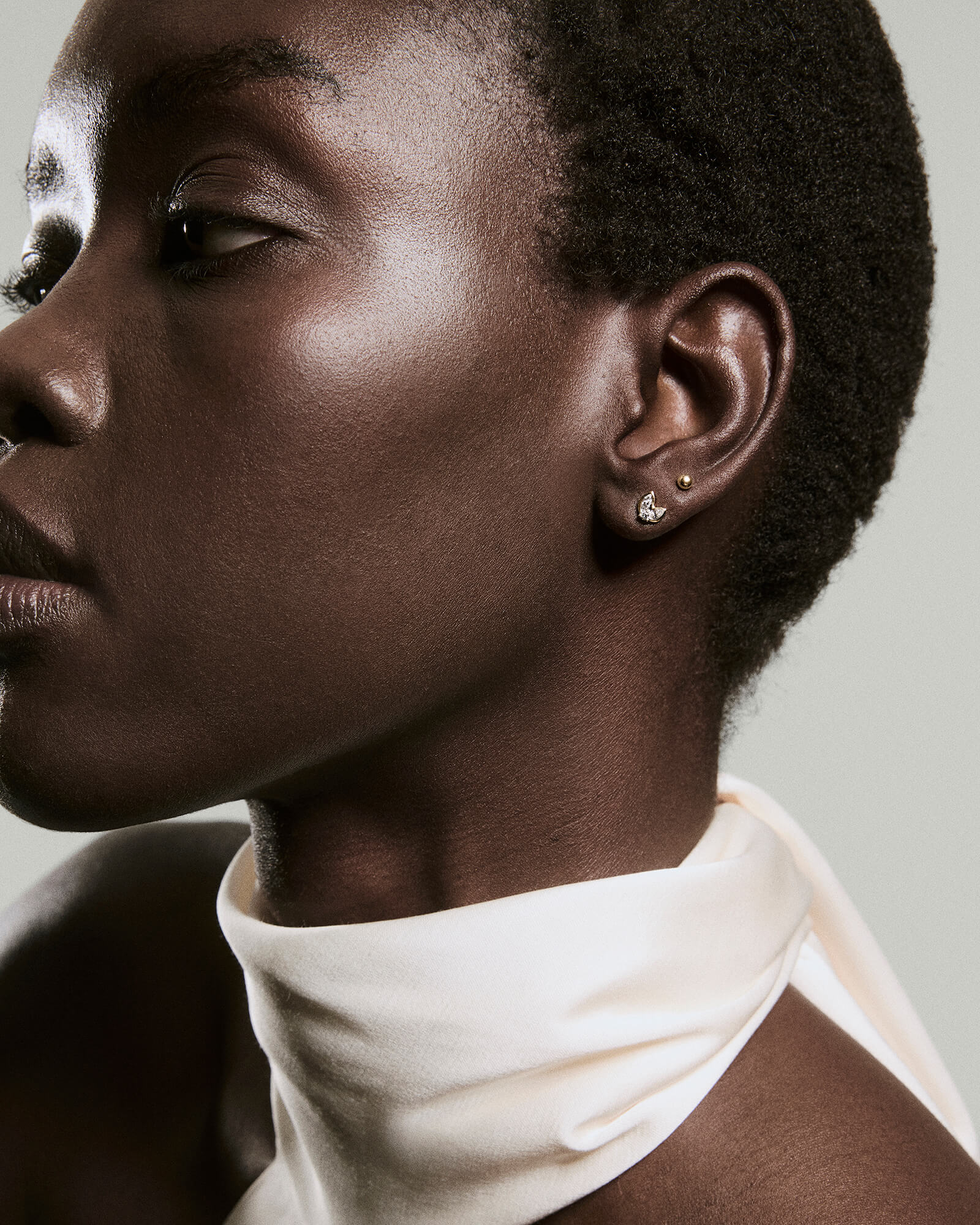 Side profile featuring Lab Grown Diamond Petal Drops, sparkling crescent-shaped studs on a person's ear, complemented by a soft white fabric draped around their shoulders.