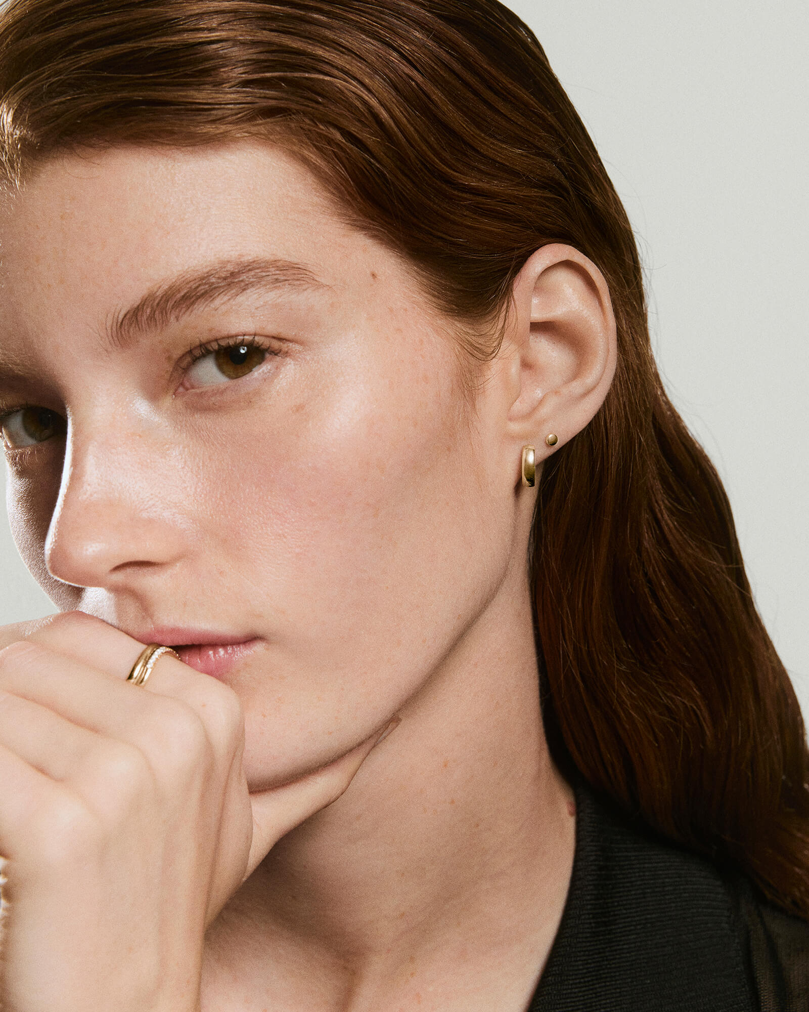 Close-up of a young woman wearing the Mini Thumbtack Flat Back Stud in 14k gold on her ear, alongside a simple hoop earring.