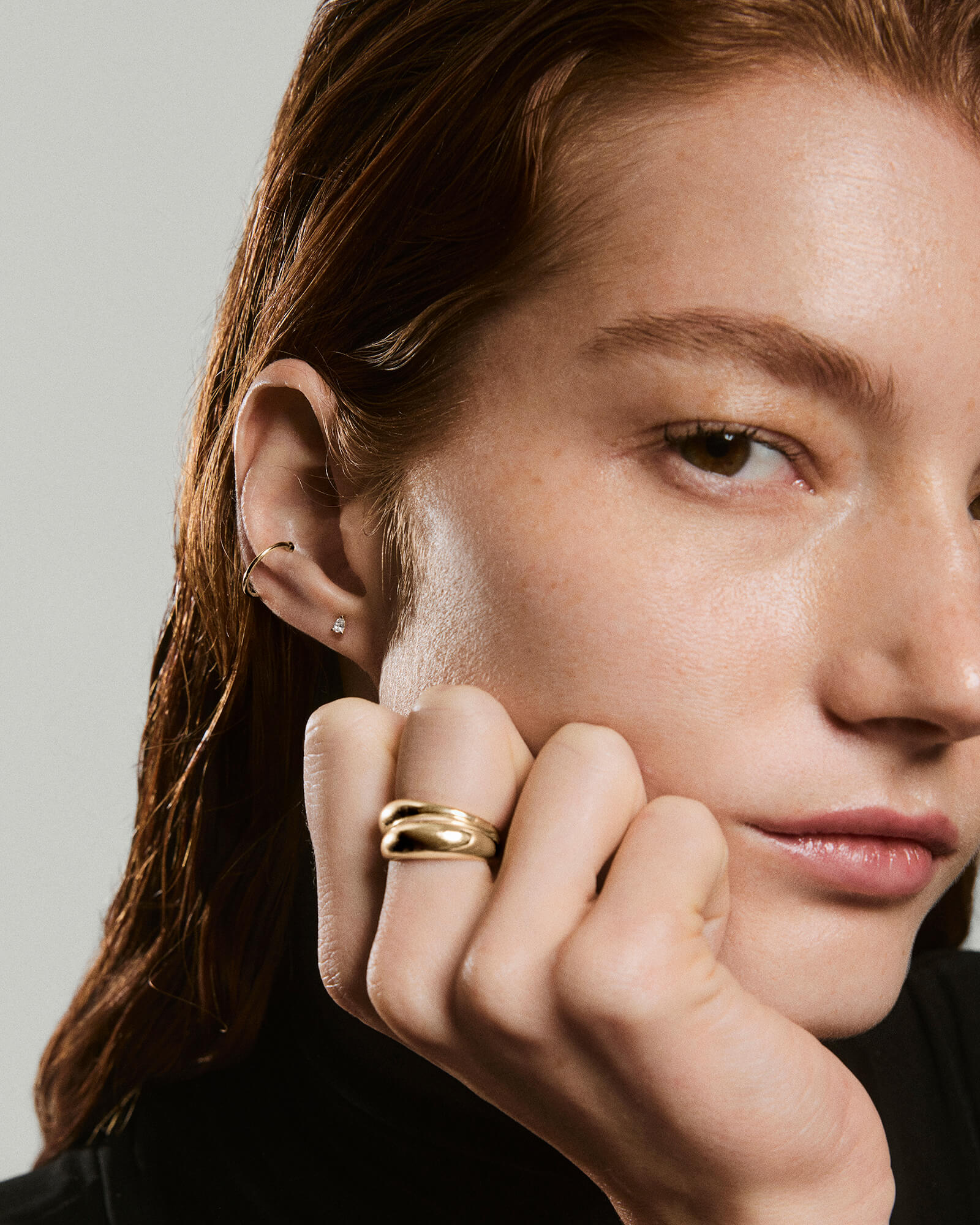 Young woman with a Pear Diamond Flat Back Stud in her ear, alongside a chunky gold ring on her finger, against a neutral background.