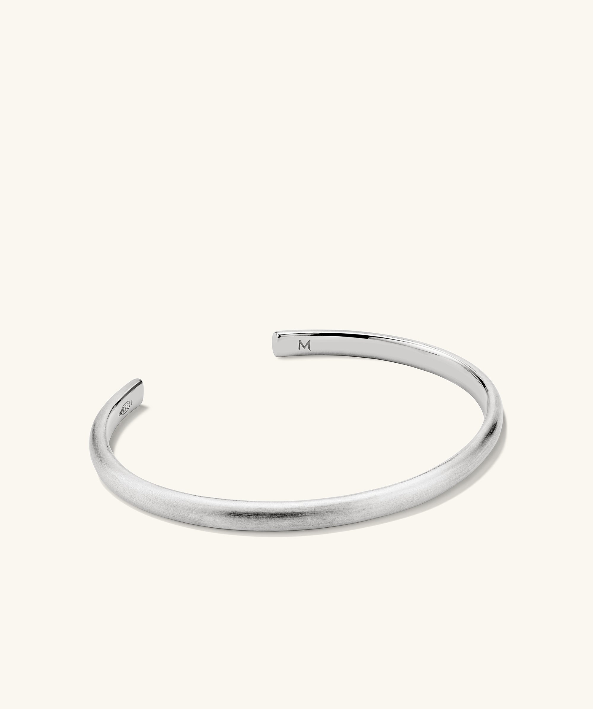 Slim Cuff: A silver bracelet with a simple silhouette, featuring a letter M charm, ideal for versatile styling.