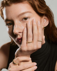 Slim Charlotte Stacker Set: close-up of gold ringsâsmooth, beaded, sapphire-accentedâon a hand, with a gold hoop earring against a freckled face.