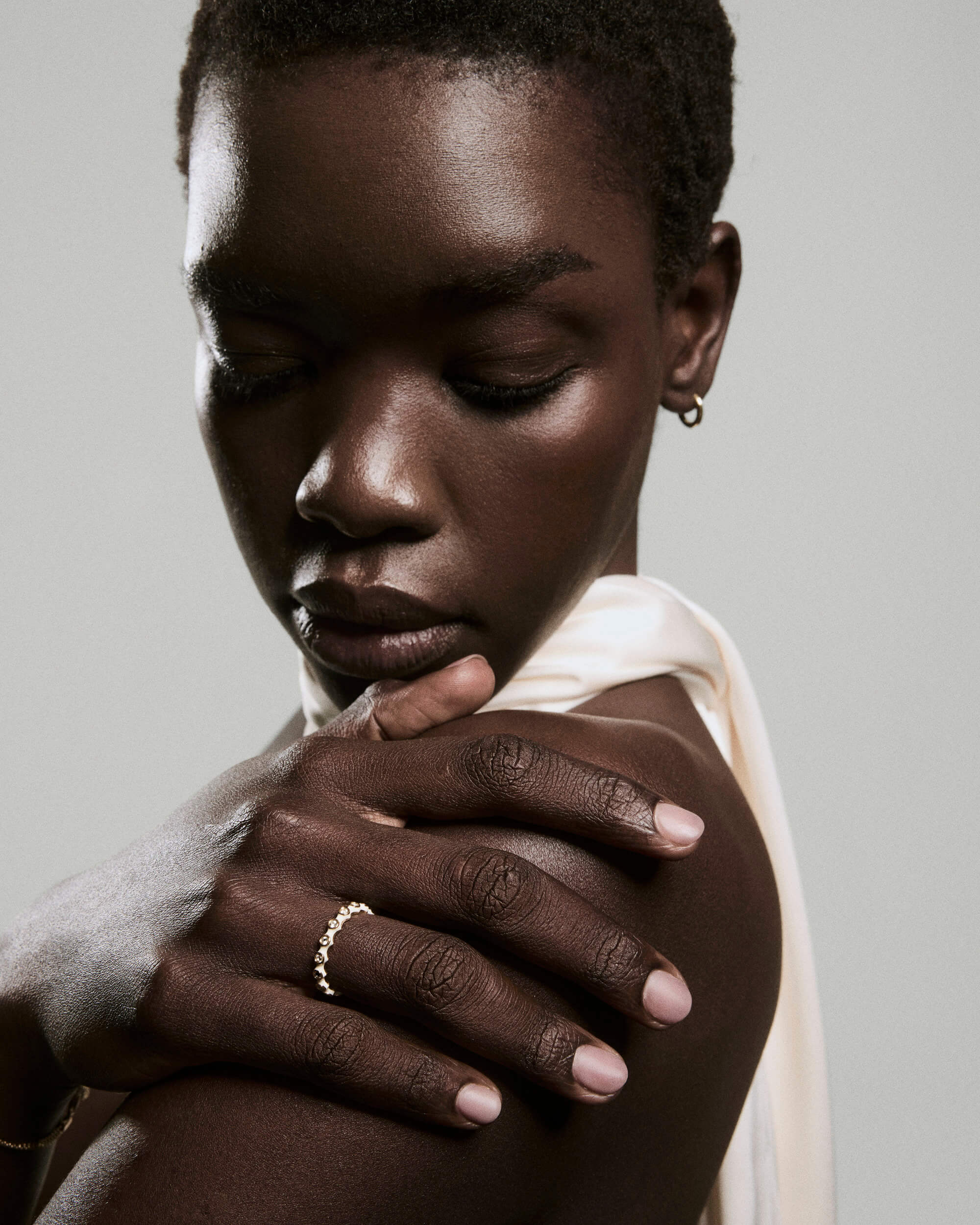 Close-up of a person wearing the Enamel Charlotte Stacker Ring, featuring linked beads, on their shoulder. A gold hoop earring complements the silky fabric.