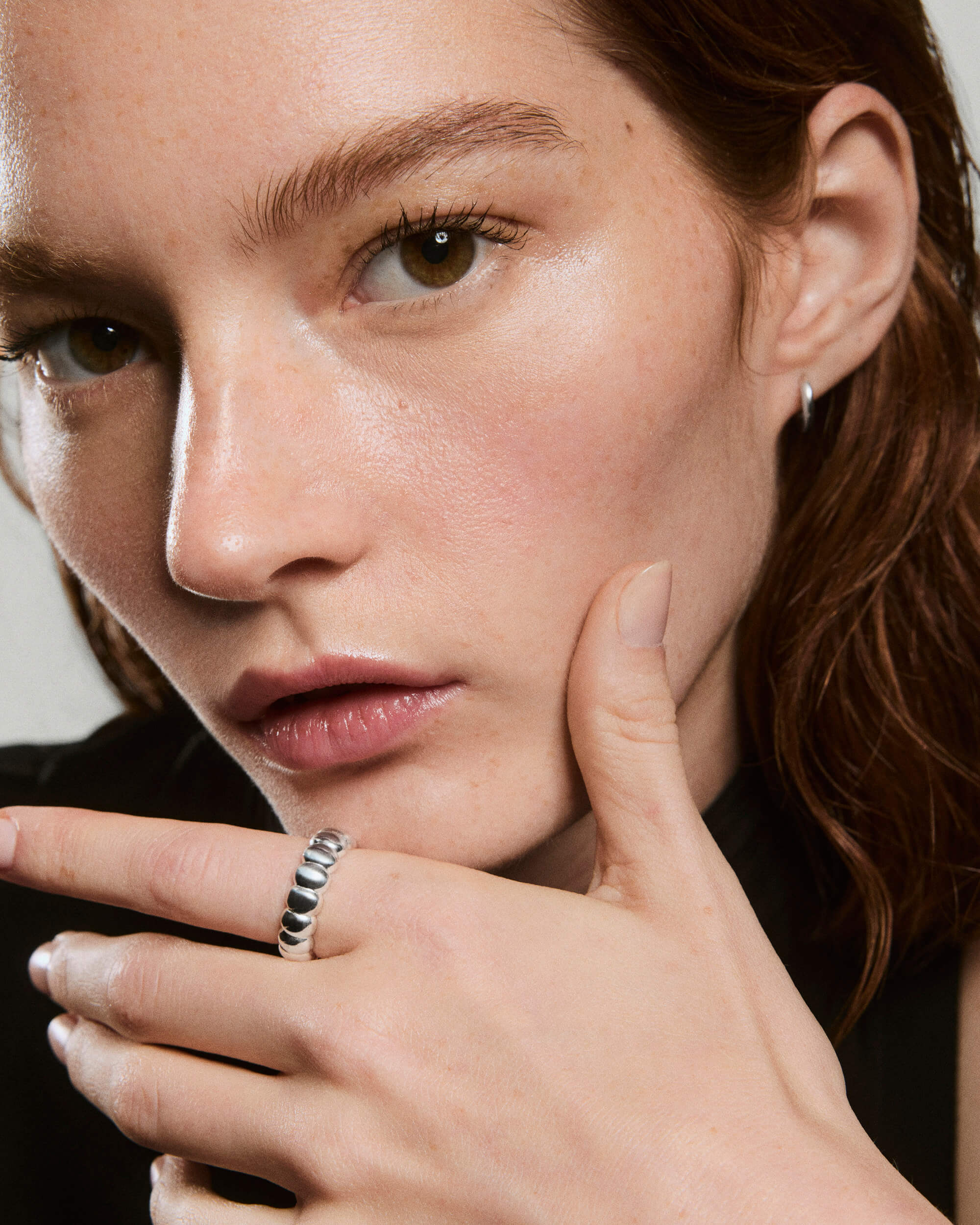 Close-up of a face and hand showcasing the Puffy Charlotte Stacker Ring, a chunky silver ring with a row of rounded beads, alongside a small silver hoop earring.