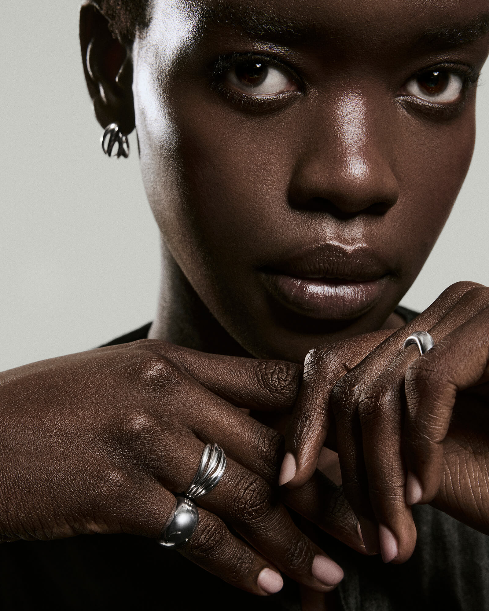 Dark-skinned person wearing the Bold Open DÃ´me Ring with sculptural silver design. Interlaced hands highlight the ring's open spaces and asymmetrical style.