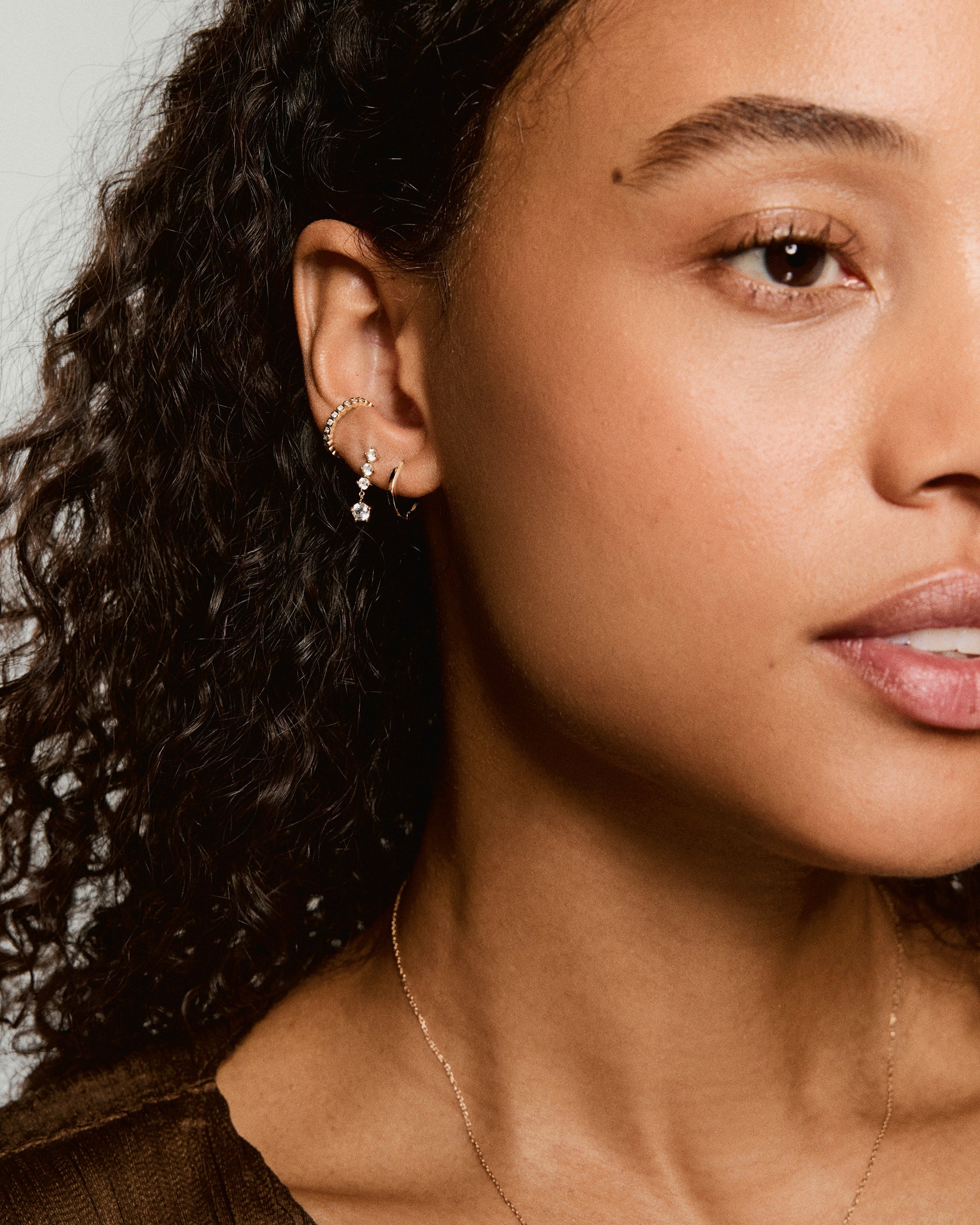 Simone Drop Earrings showcased on a woman's ear, featuring a delicate drop with graduated crystals and a gold hoop, complemented by a fine gold chain necklace.