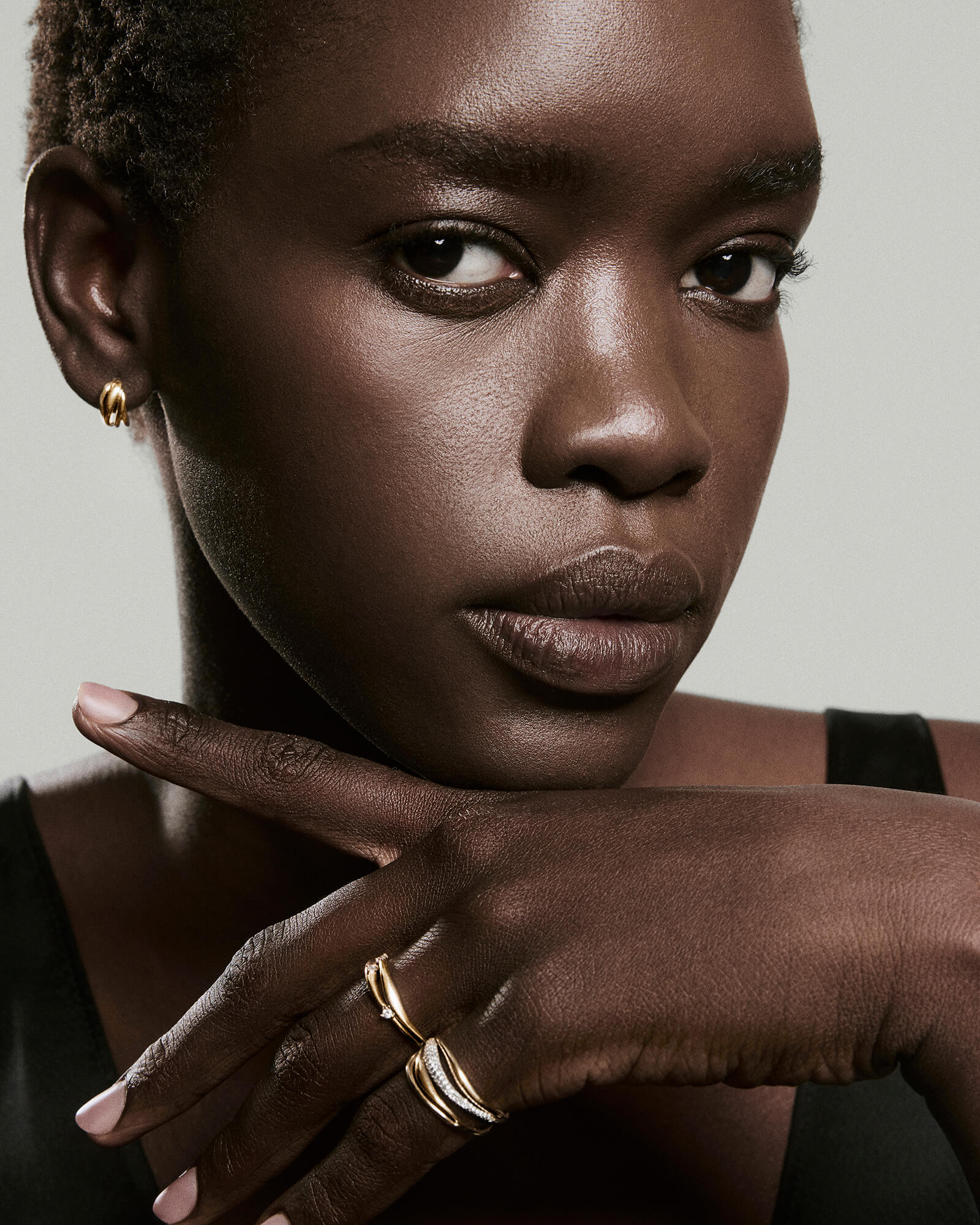 Black woman with gold hoop earring showcases Open DÃ´me Diamond Ring on raised hand, featuring sculptural design and trio of diamonds in 14k Salmon GoldTM.