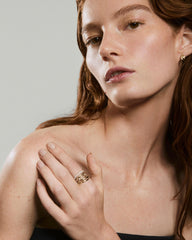 Young woman gently touches her shoulder, showcasing the Open DÃ´me Ring, a stackable gold ring set with a diamond, highlighting its elegant design and ethical sourcing.