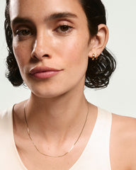 Young person wearing the Mini Serpentine Necklace, featuring light S-curve links, paired with small gold hoop earrings, showcasing sleek design and subtle shine.