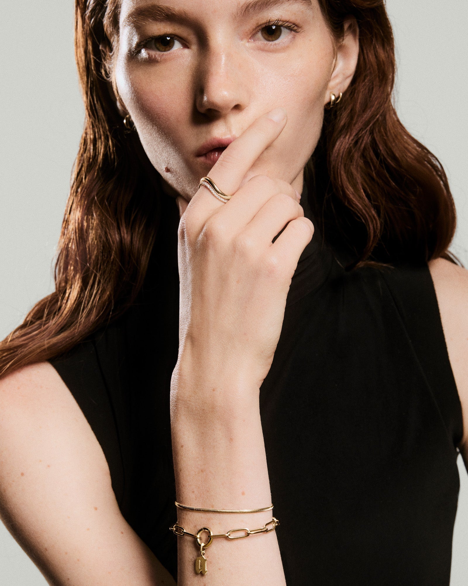 Young woman wearing Paperclip Chain Charm Bracelet, featuring a chunky link design with a small charm, paired with other elegant gold jewelry.