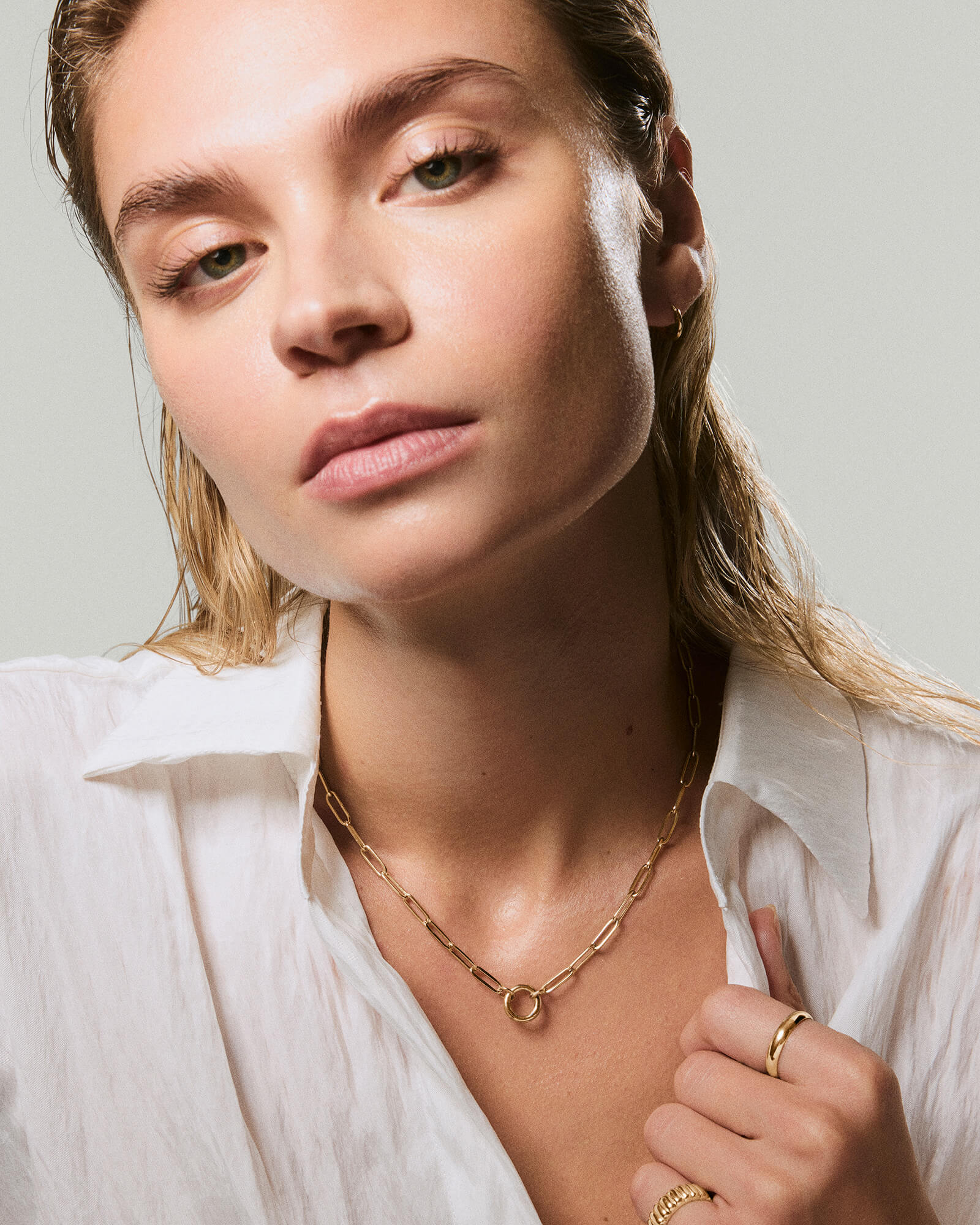 Close-up of a woman wearing a Paperclip Chain Charm Necklace with a front clasp, complemented by gold hoop earrings and rings, conveying understated elegance.