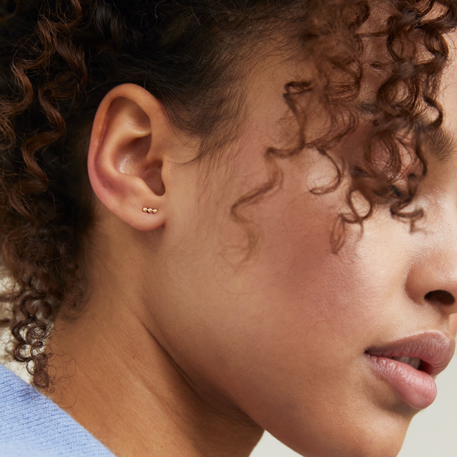 Close-up of a woman showcasing Spheres Bar Studs in her ear, highlighting the handcrafted 14k solid gold jewelry.