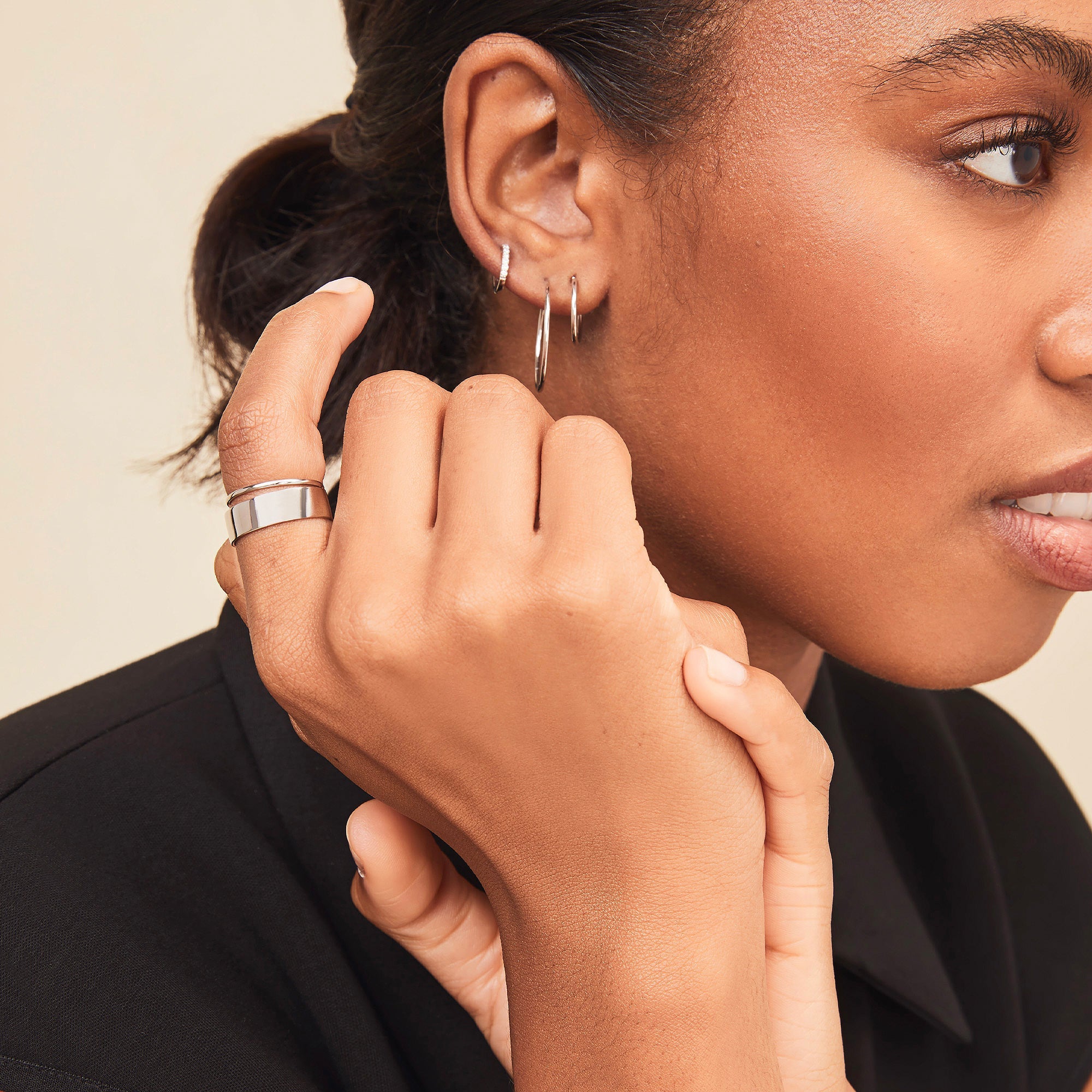 Close-up of a woman's hand wearing the Daily Stacker Ring, highlighting its elegant design, with earrings and makeup subtly visible in the background.