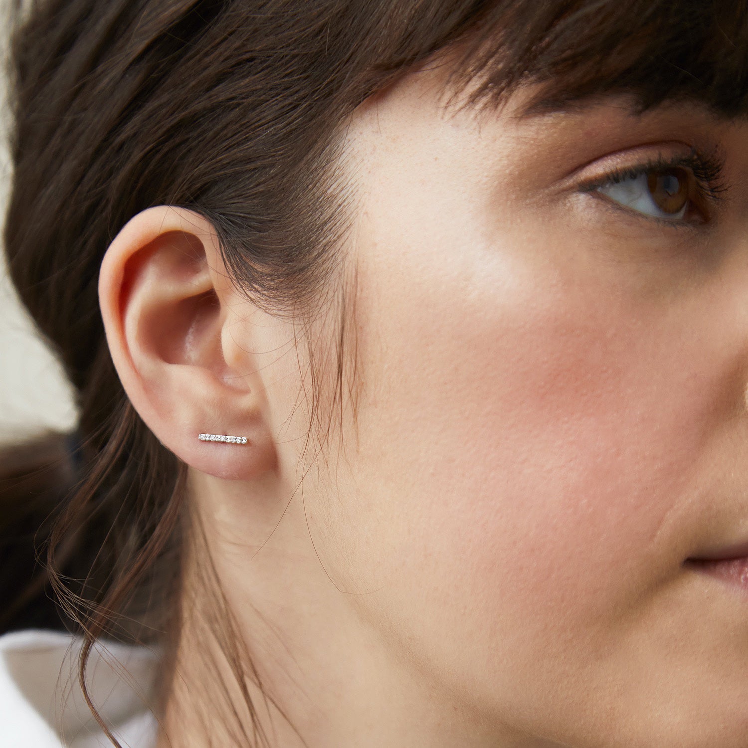 Close-up of a woman's ear wearing PavÃ© Diamonds Long Bar Studs, handcrafted in 14k solid gold and set with diamonds.