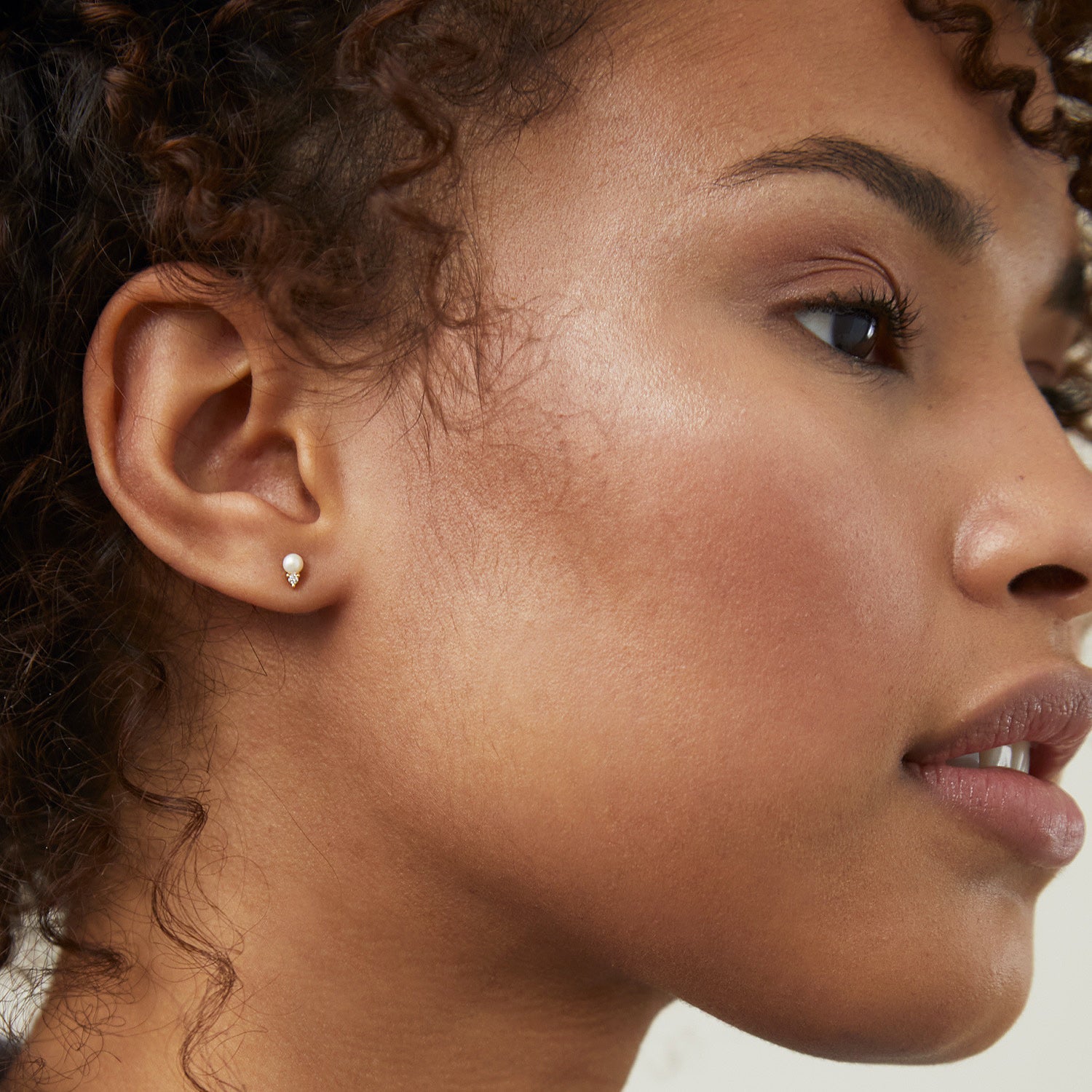 Diamond Pearl Studs on a woman's earlobe, showcasing 14k solid gold craftsmanship with diamonds and a pearl, highlighting the sleek and elegant design.