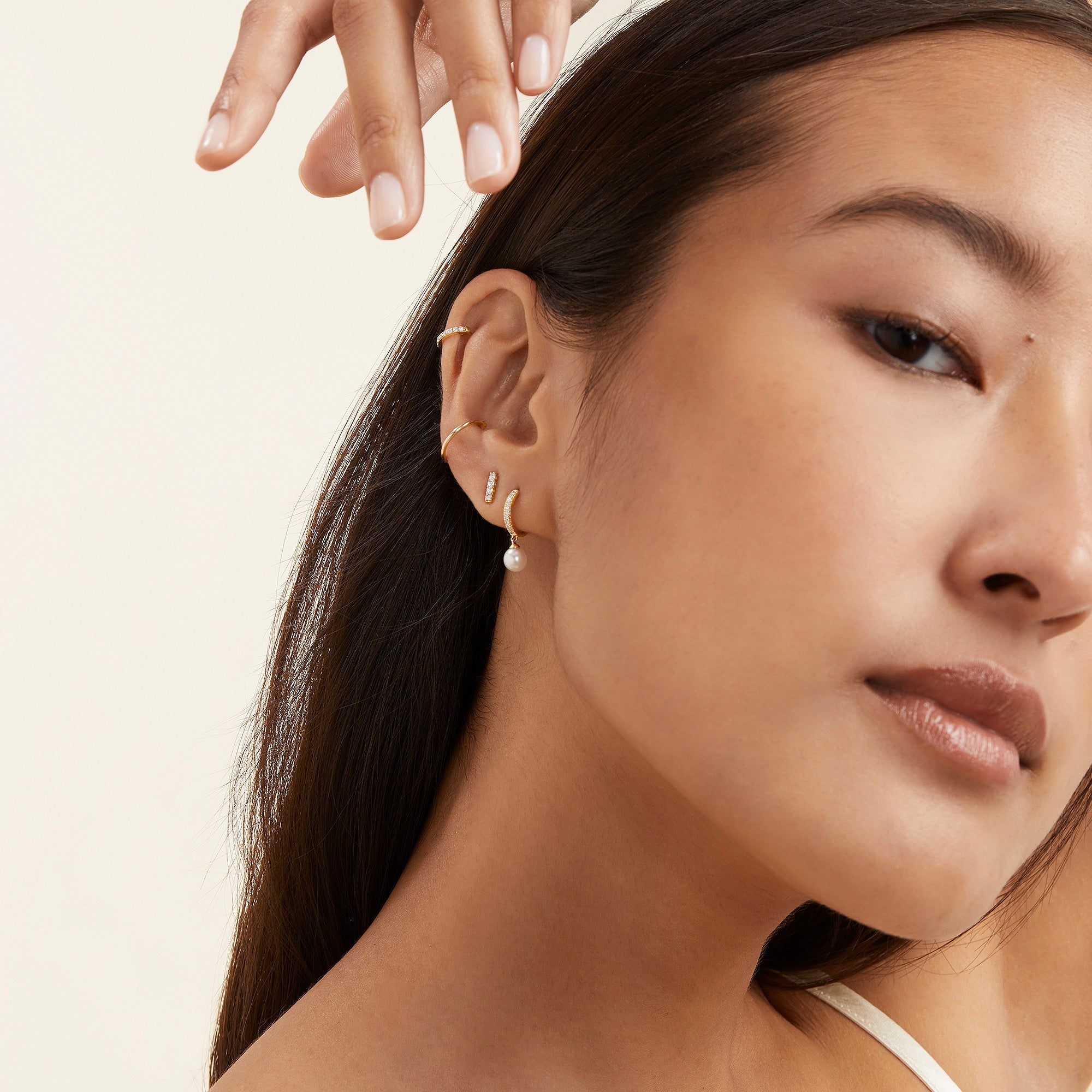 Woman wearing PavÃ© Diamond Pearl Huggies, featuring 22 pavÃ©-set diamonds and a round freshwater pearl, hand on head, showcasing earrings.