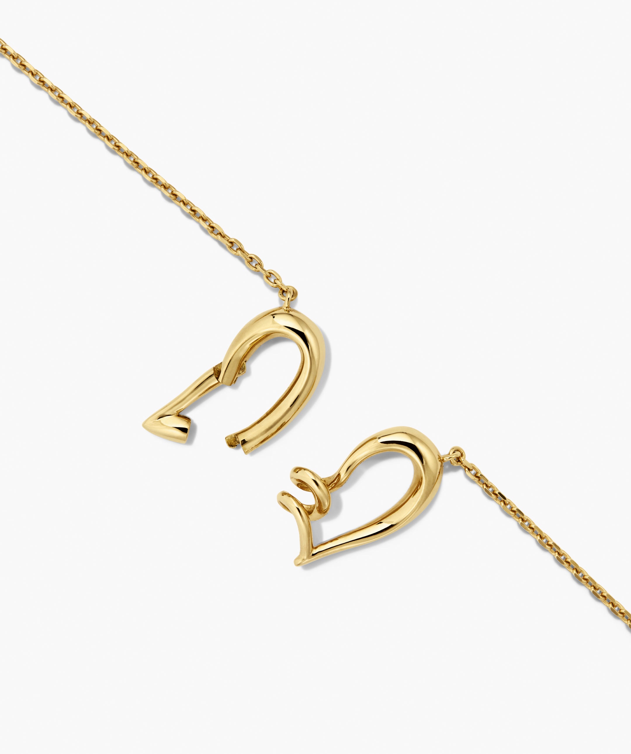 Heart to Heart Necklace featuring two gold-tone chains with interlocking abstract open-heart clasps, forming a modern sculptural heart when connected.