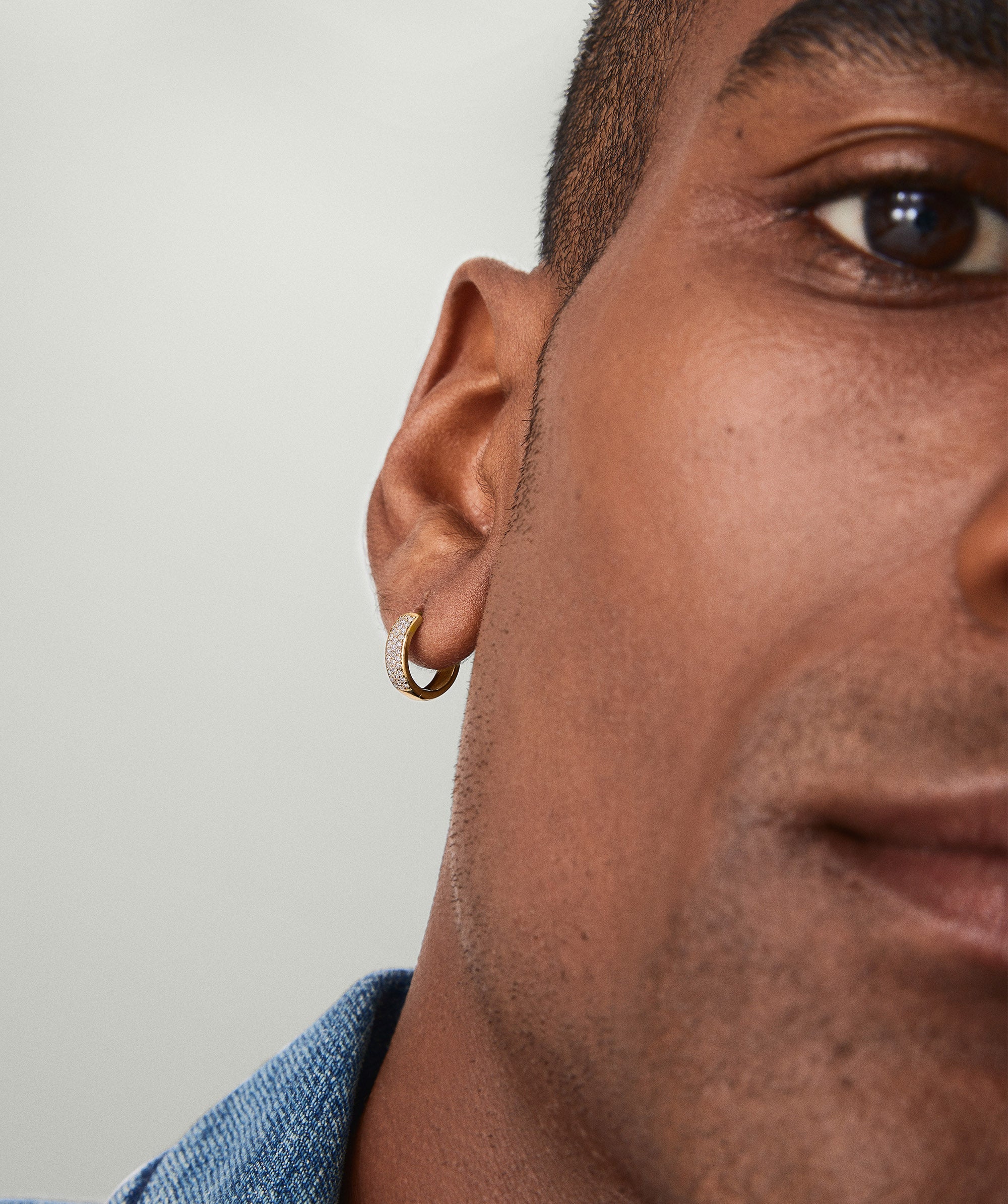Close-up of a man's ear wearing Bold PavÃ© Diamond Huggie Hoops, crafted in 14k solid gold with responsibly sourced diamonds.