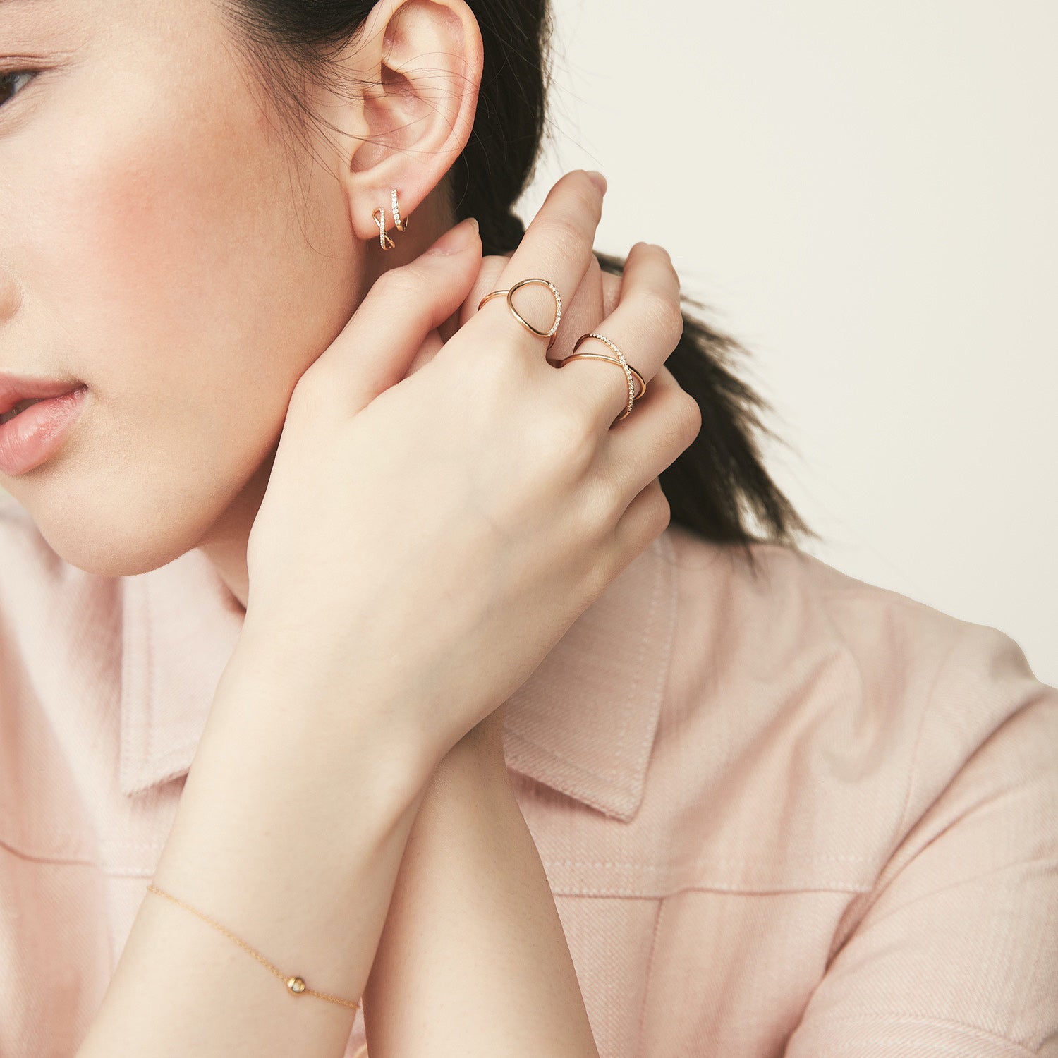 A woman wearing a pink shirt showcases the PavÃ© Diamond X Ring, a 14k solid gold ring with pavÃ© diamonds, highlighting its elegant X-shaped design on her finger.