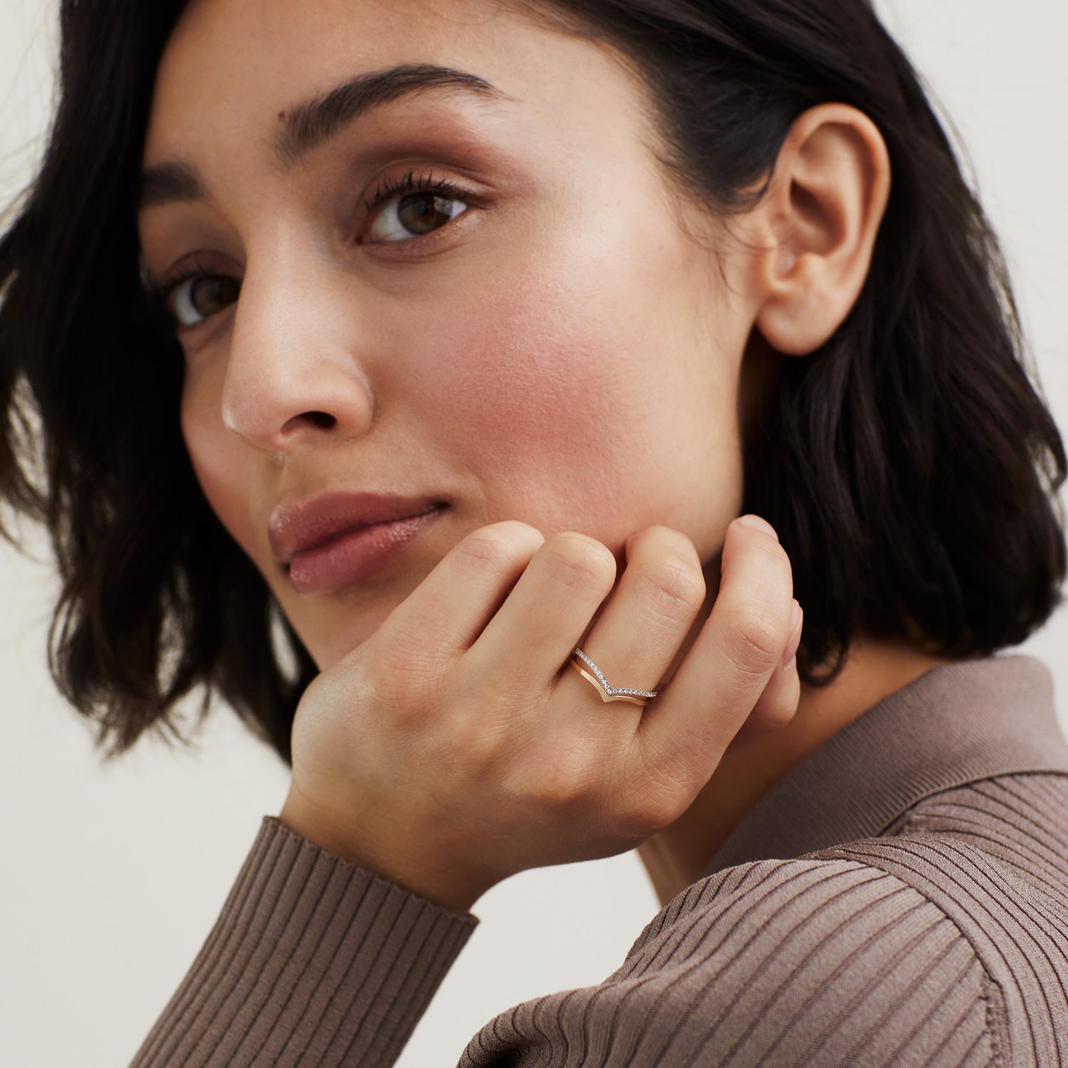 Woman resting her chin on her hand, showcasing the Wishbone Ring, a handcrafted 14k solid gold piece, worn on her finger.